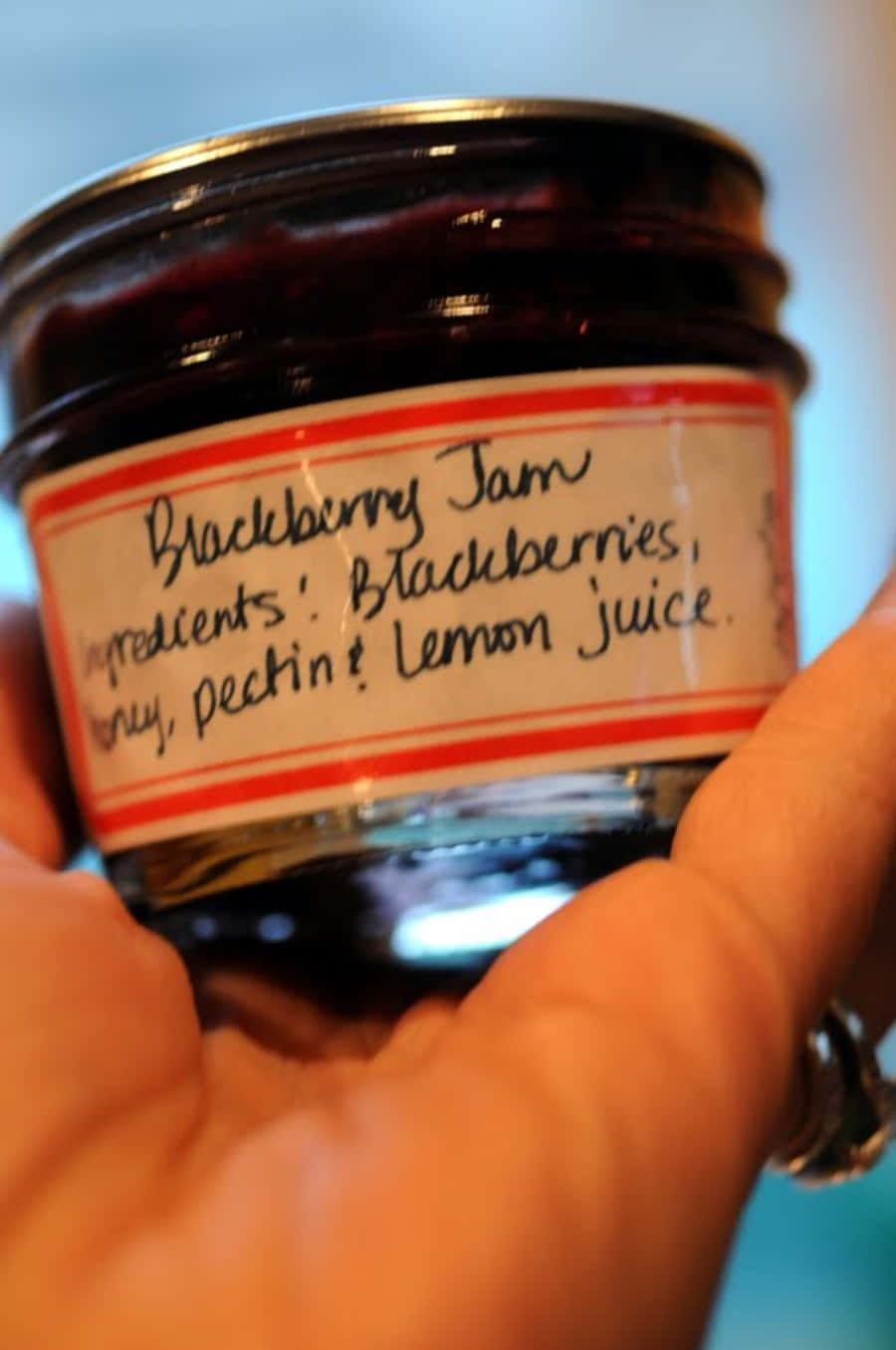 Blackberry Jam 桌布 壁紙 — 一隻手拿著一罐自製黑莓果醬，上面有手寫標籤列出成分。
