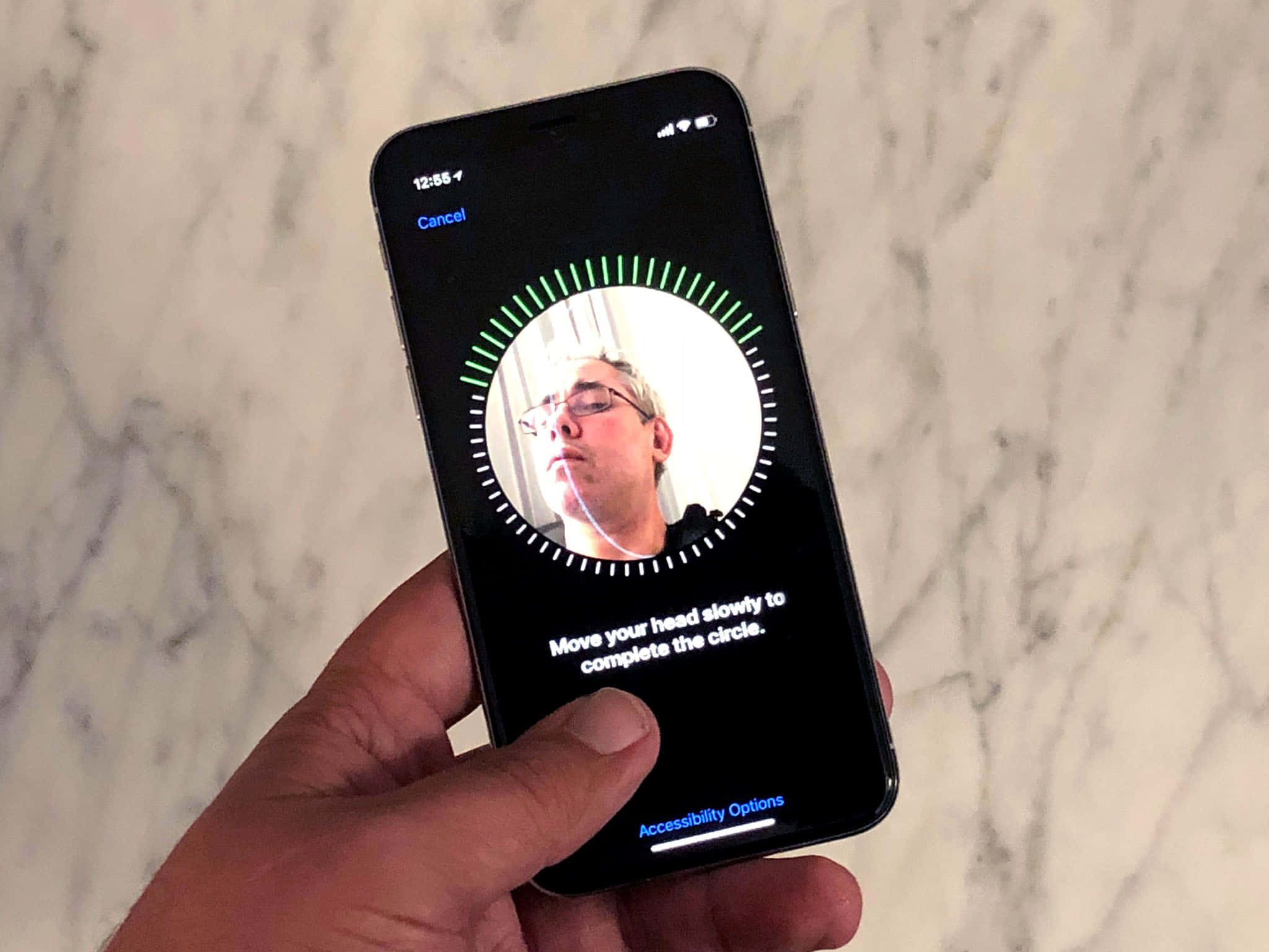 Face Id 桌布 壁紙 — 一隻手拿著一部智能手機，在大理石背景上顯示無障礙面部追蹤功能。