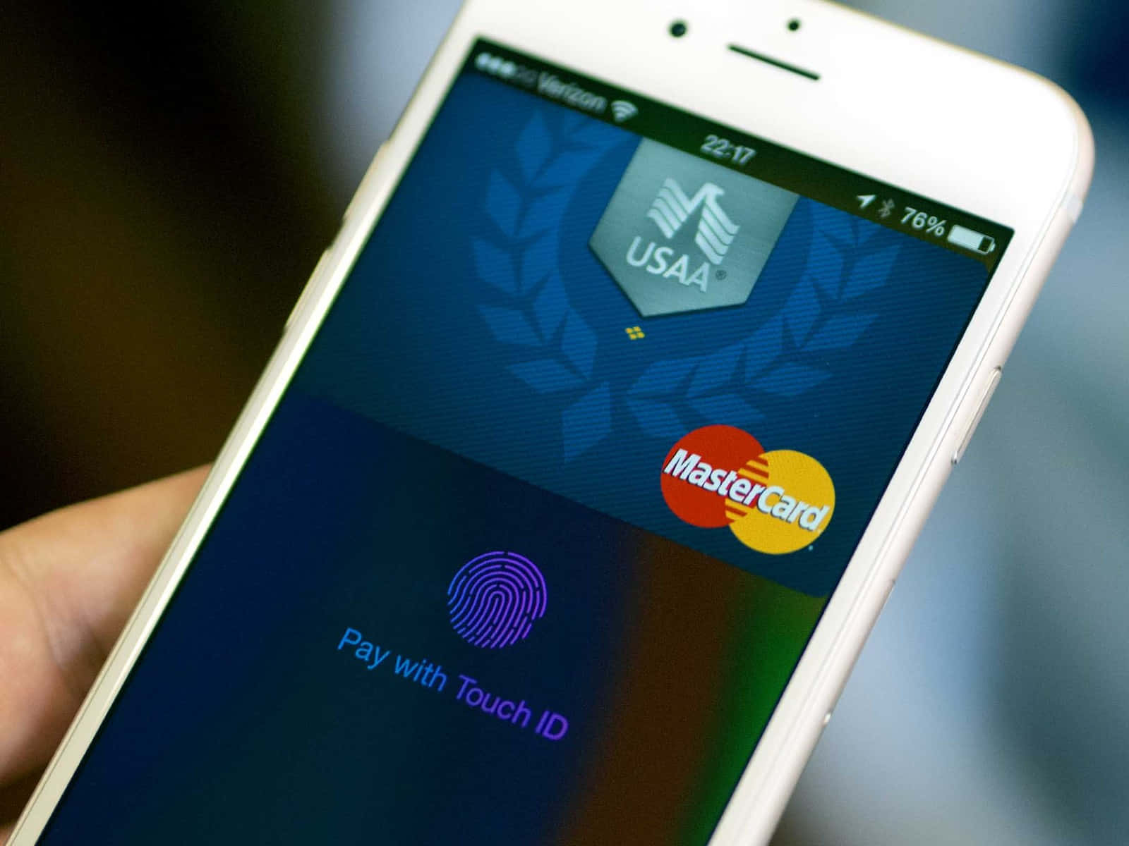 Touch Id 桌布 壁紙 — 一隻手拿著一部白色iPhone，顯示USAA MasterCard付款畫面及Touch ID提示，背景模糊。