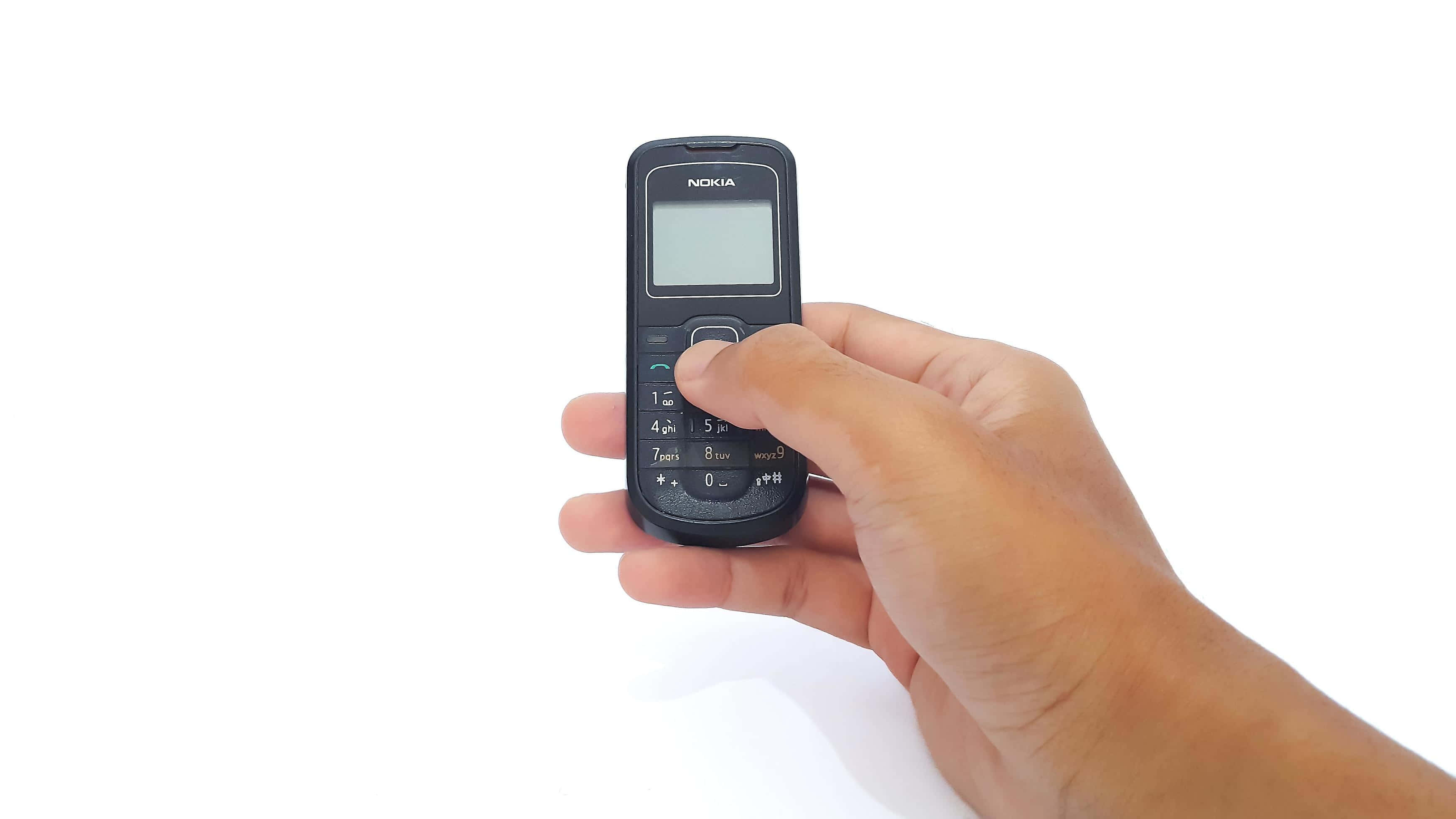 Nokia 桌布 壁紙 — 一隻手拿著一部黑色Nokia功能手機，背景為純白色，拇指按著一個按鈕。