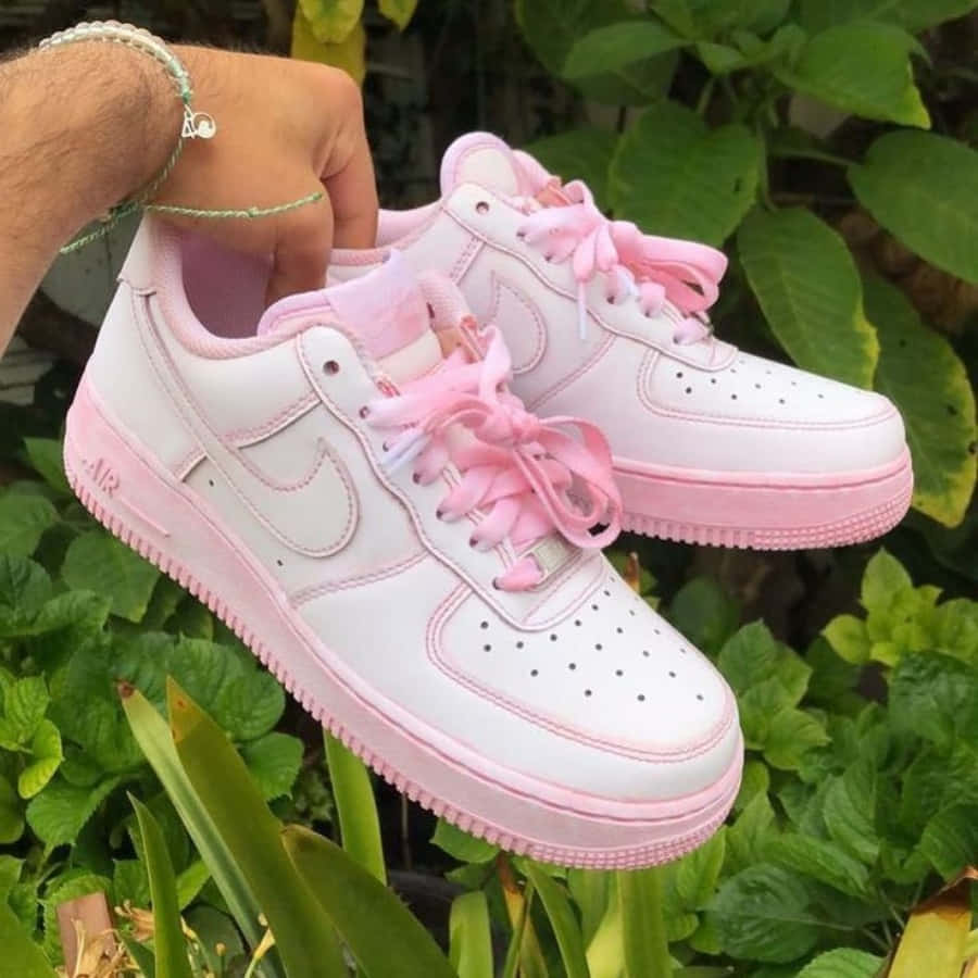 Pink Shoes 桌布 壁紙 — 一隻手拿著一雙粉紅色和白色的Nike Air Force 1運動鞋，背景是茂密的綠色樹葉。