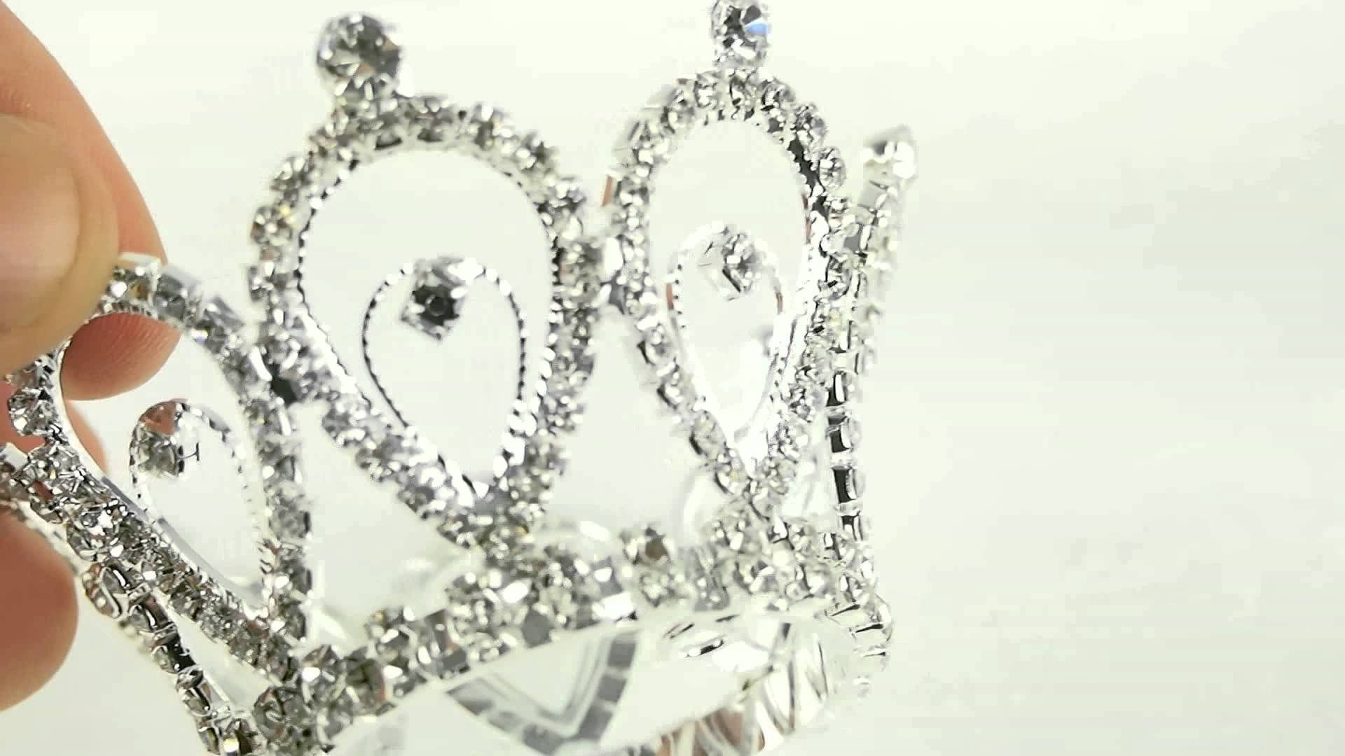 King And Queen 桌布 壁紙 — 一隻手拿著一頂閃閃發光的銀色頭飾，上面鑲嵌著水晶，背景是明亮的白色。