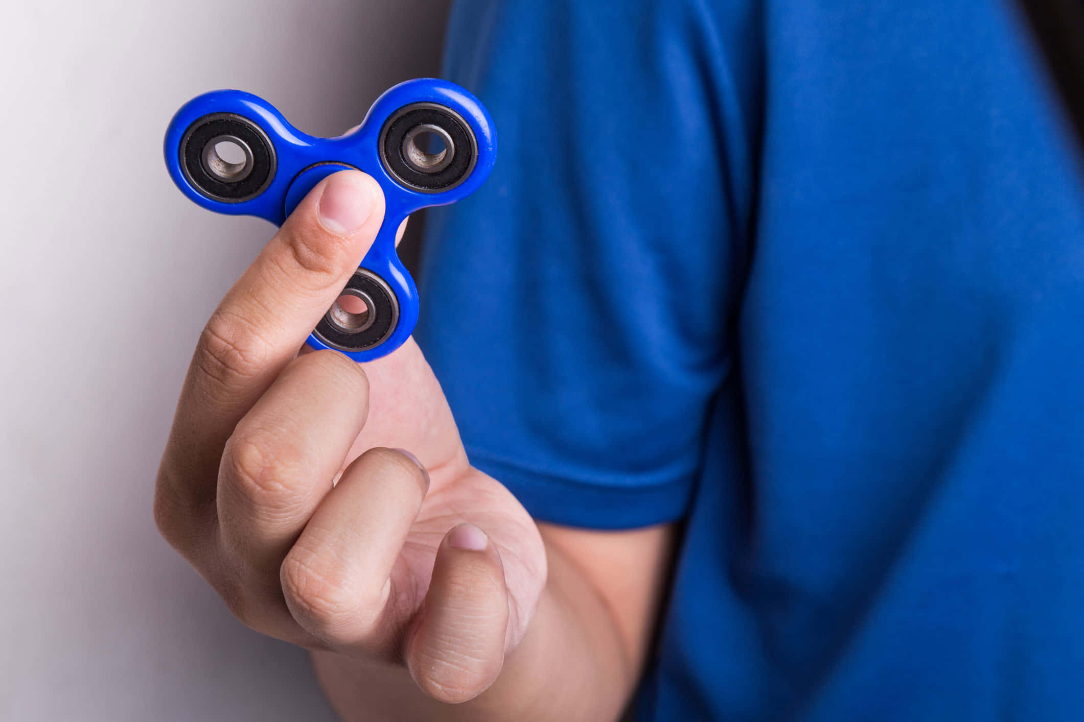 Fidget 桌布 壁紙 — 一隻手拿著亮藍色指尖陀螺的特寫，背景為純色。
