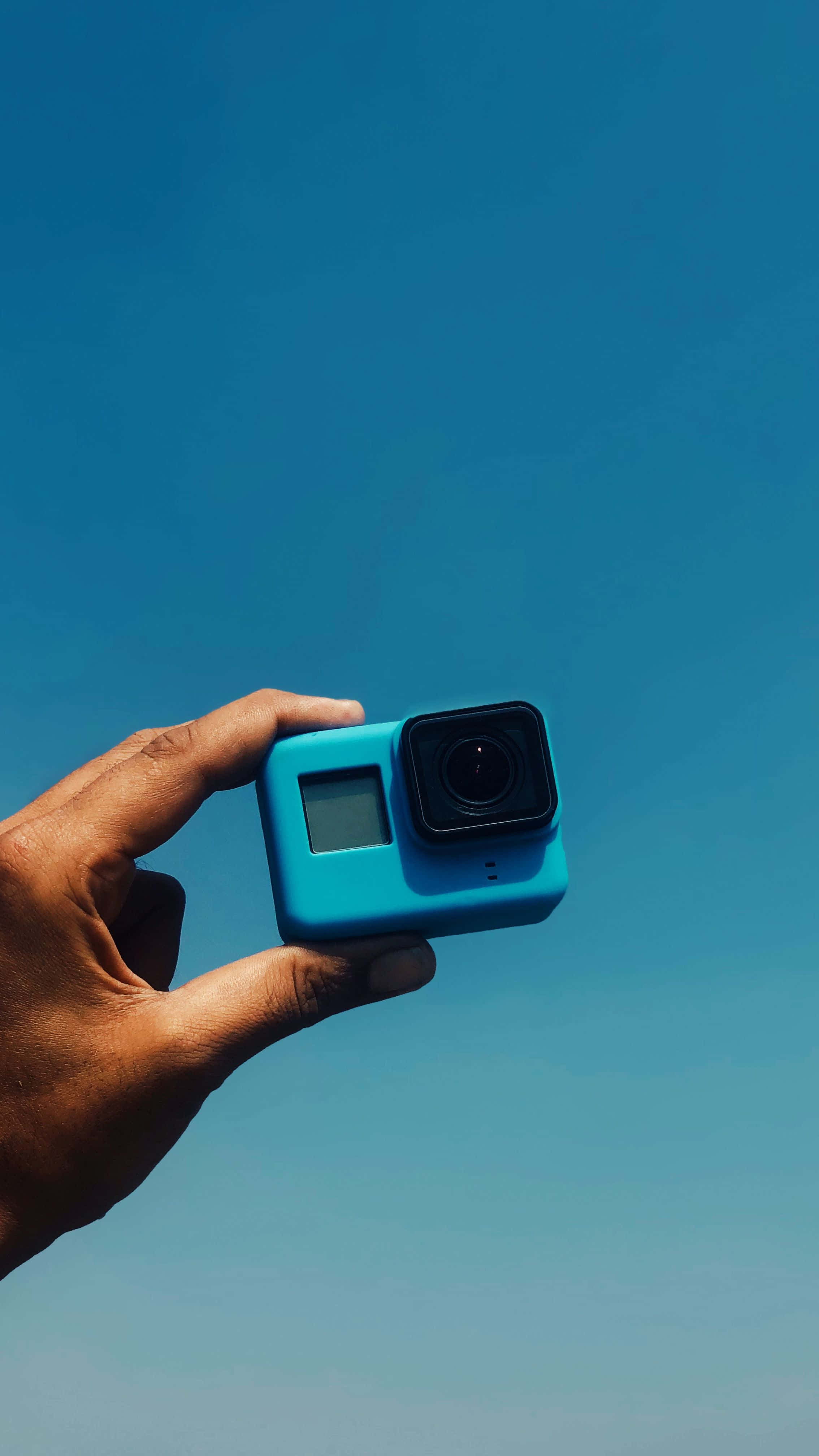 gopro 桌布 壁紙 — 一隻手拿著亮藍色運動相機，背景是清澈的藍天。