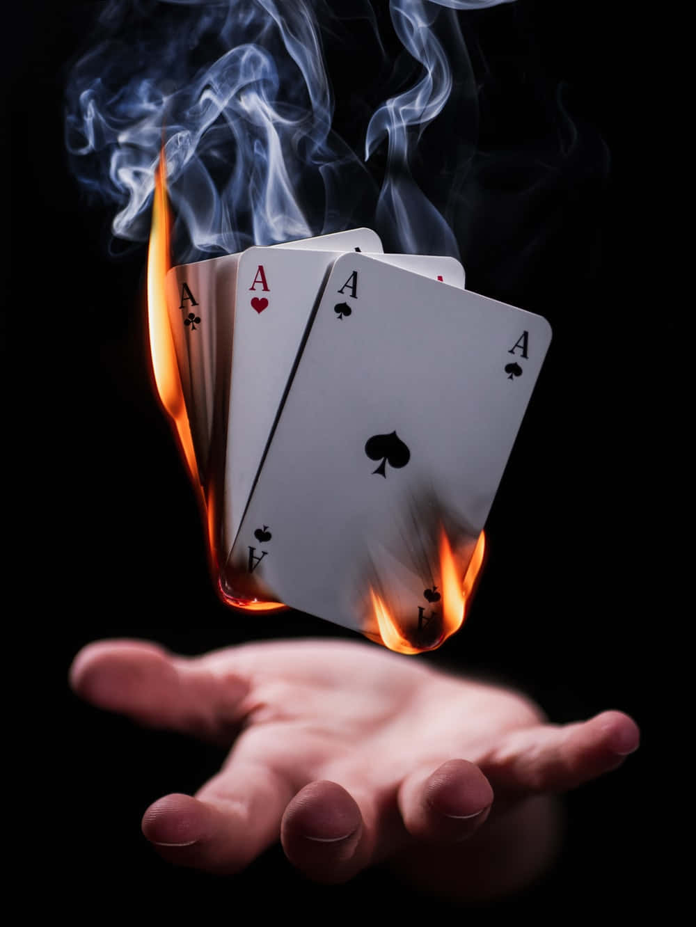 Card Games 桌布 壁紙 — 一隻手拿著四張燃燒的Ace撲克牌，煙霧在黑色背景上升起。