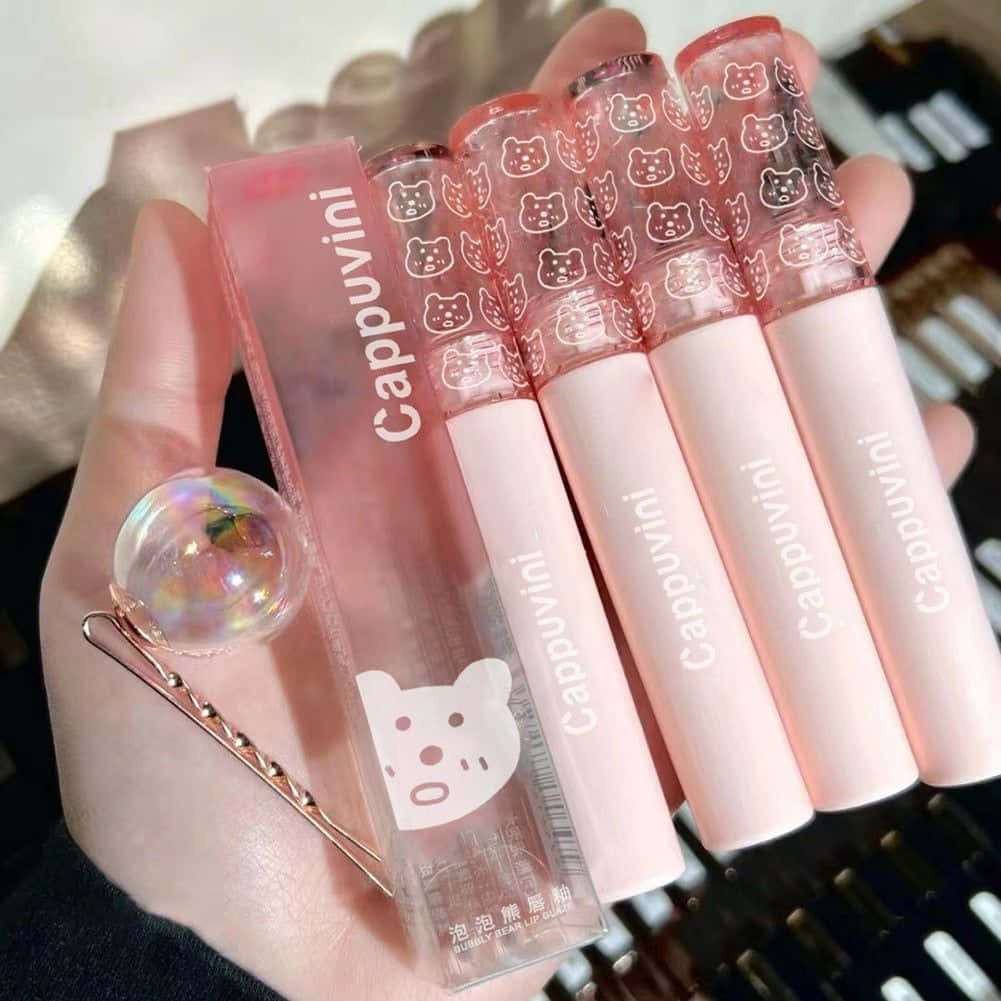 lipstick 桌布 壁紙 — 一隻手拿著四支粉紅色貓咪主題唇彩和一個相配的盒子，旁邊還有一個全息髮夾。