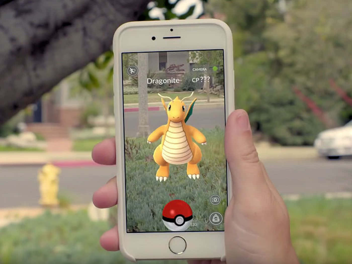 Pokemon Virtual World 桌布 壁紙 — 一隻手拿著智能手機，顯示Pokemon GO中的虛擬Dragonite，疊加在郊區草坪上，背景有樹木和消防栓。