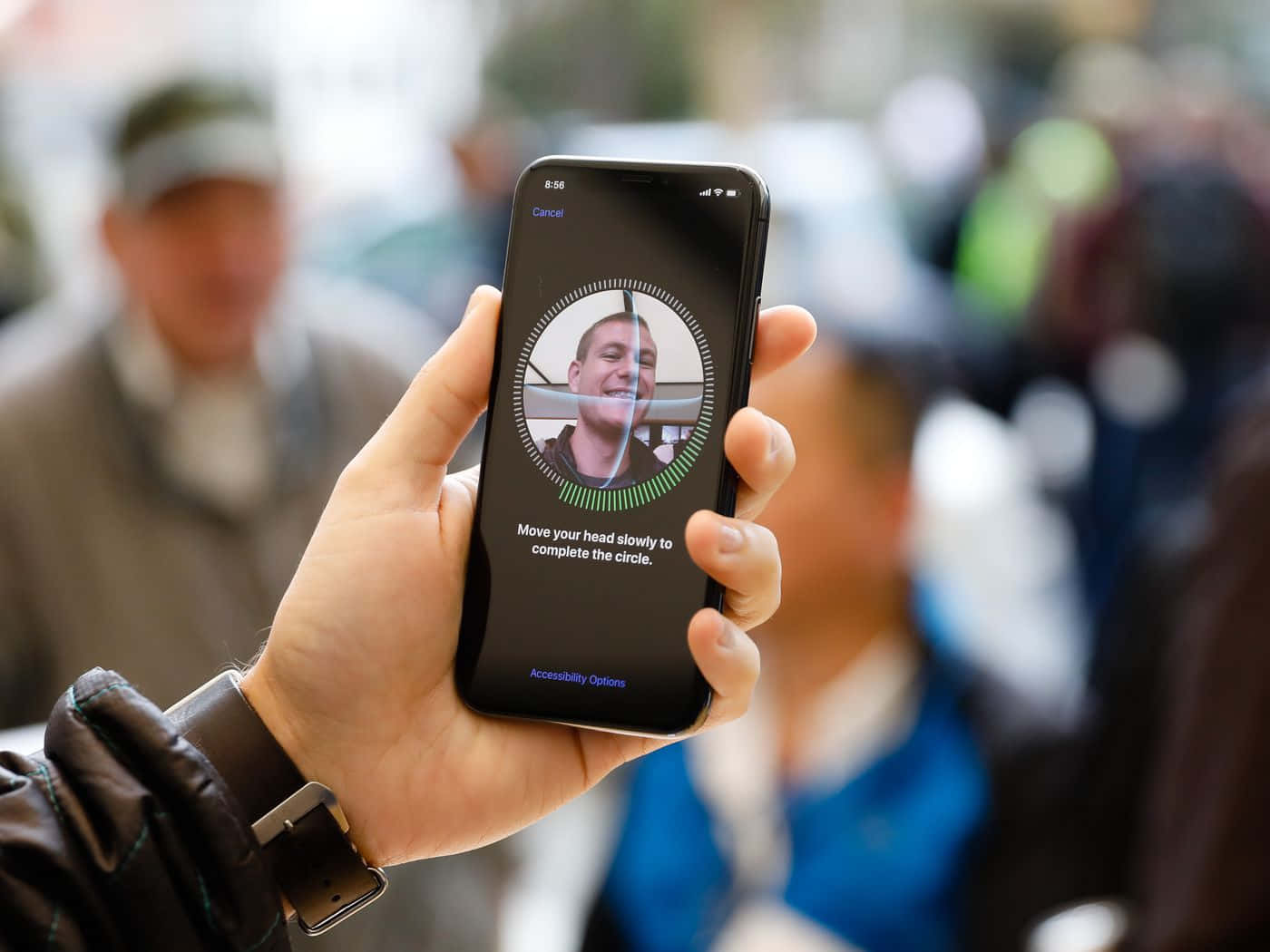 Face Id 桌布 壁紙 — 一隻手拿著智能手機，顯示人臉識別設置畫面，上面有一個微笑的男士臉孔和指示緩慢移動頭部。