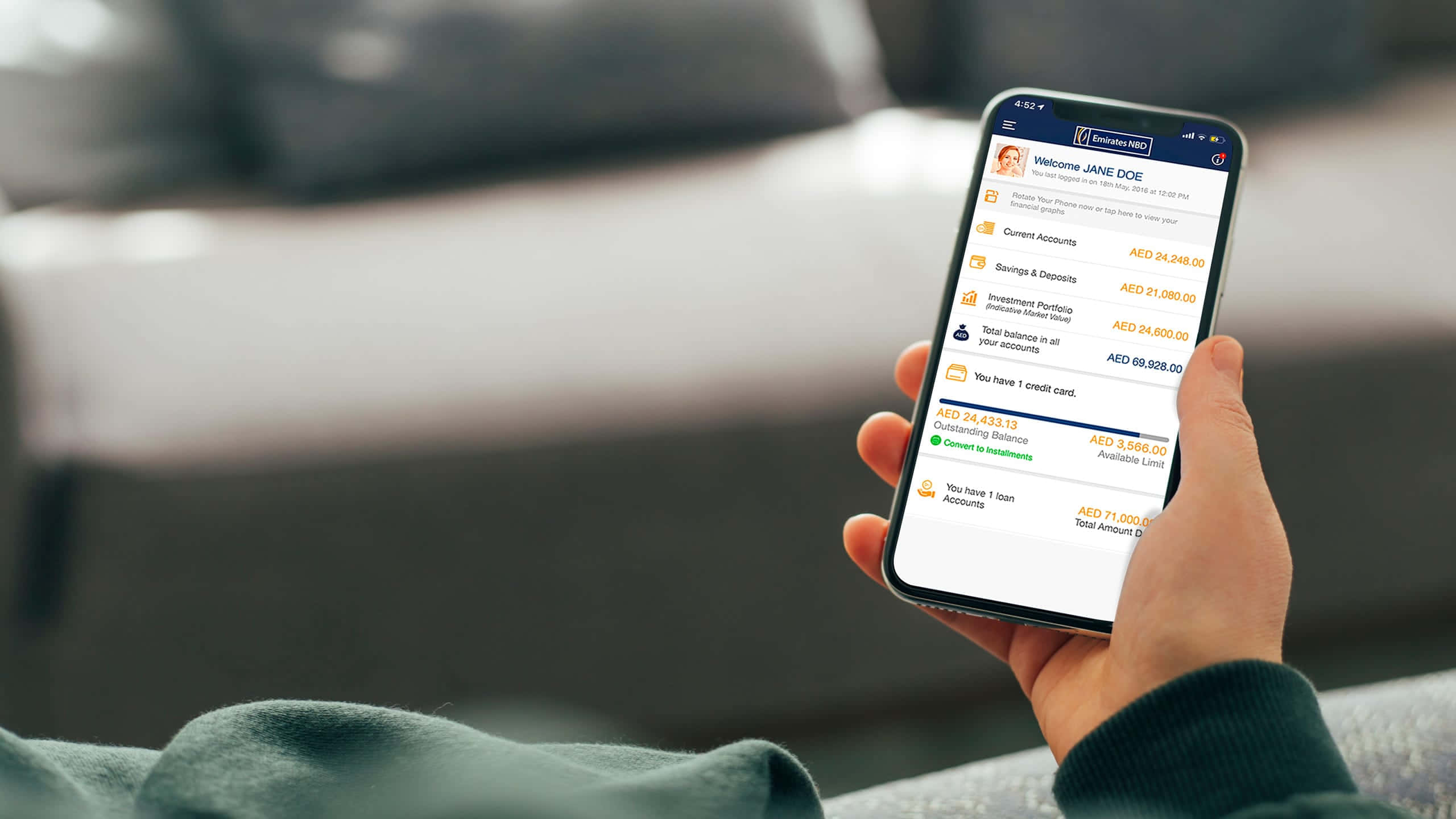 Mobile Banking 桌布 壁紙 — 一隻手拿著智能手機，顯示銀行應用程式，包含帳戶結餘和財務詳細資訊，背景是模糊的沙發。