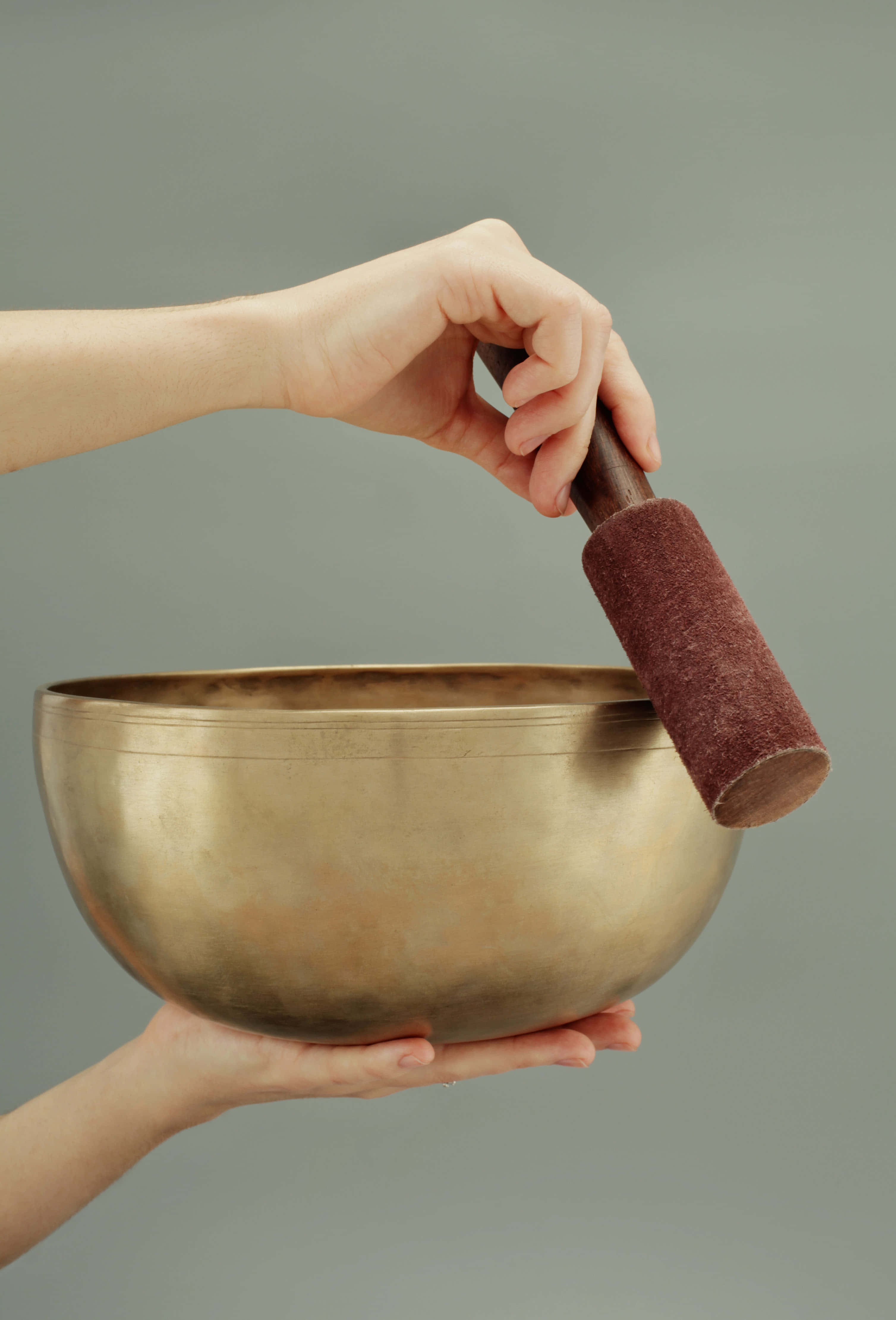 Reiki 桌布 壁紙 — 一隻手拿著黃銅頌缽，另一隻手舉起帶軟墊的敲棒，準備敲擊缽邊。