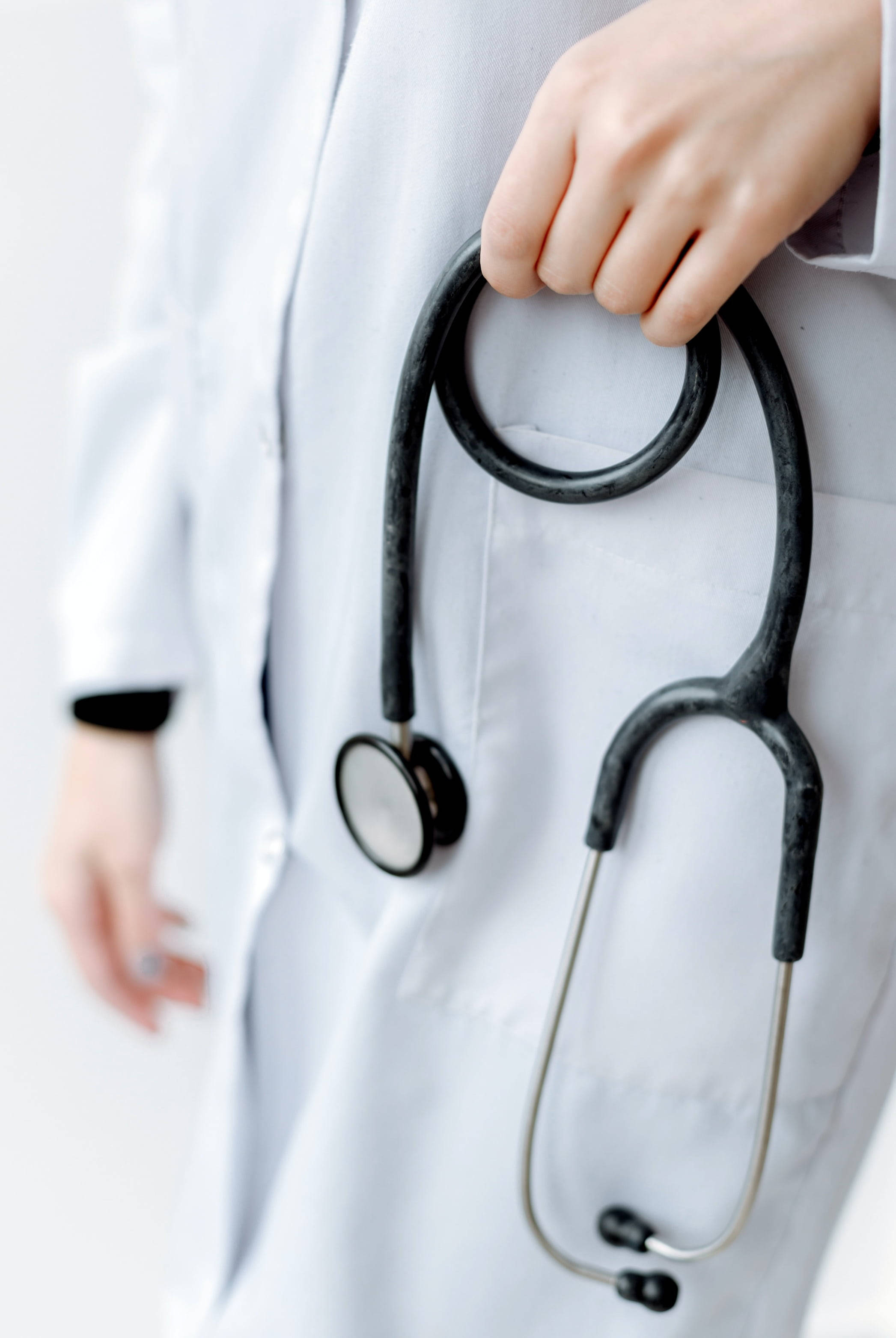 Stethoscope 桌布 壁紙 — 一隻手拿著黑色聽診器貼在白色醫生袍上的特寫，光線柔和。