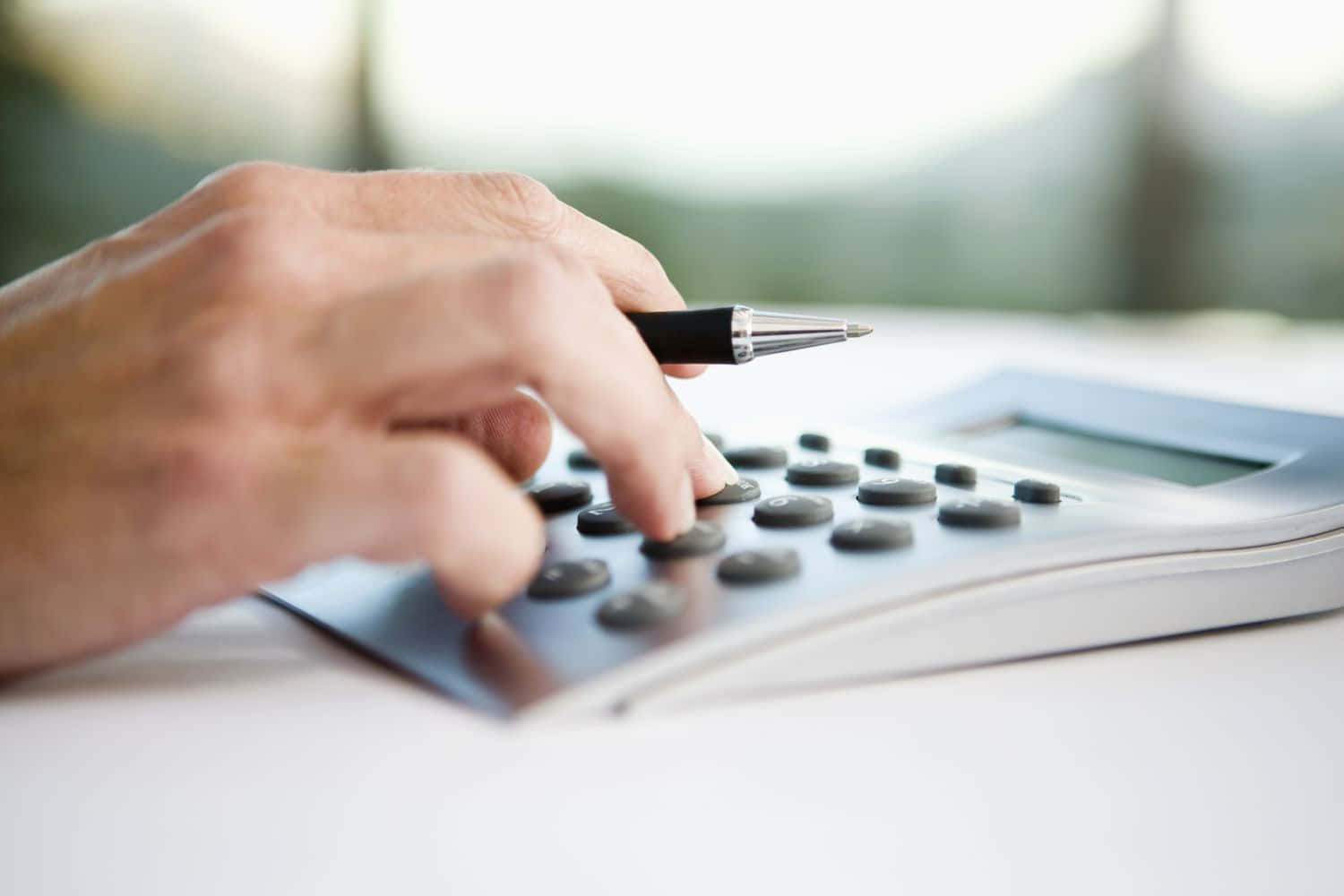 Calculator 桌布 壁紙 — 一隻手按住銀色計算機上的按鈕，同時握著筆的特寫。