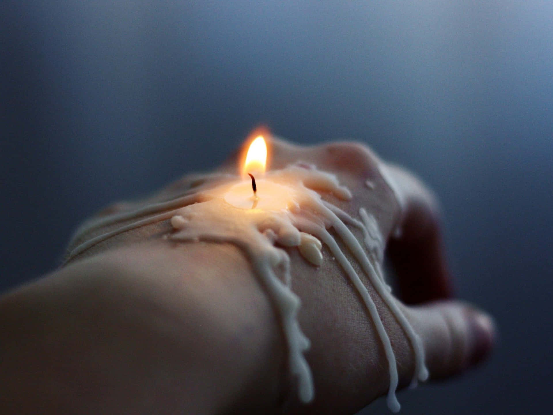 Burn 桌布 壁紙 — 一隻手捧著正在融化的蠟燭，蠟油滴落在手腕上，背景是柔和的藍色。