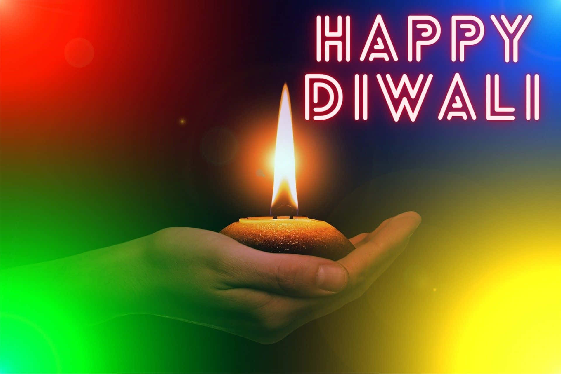Happy Diwali 桌布 壁紙 — 一隻手捧著發光的迪亞蠟燭，背景是鮮豔的彩虹漸變色，並有發光霓虹文字「HAPPY DIWALI」。