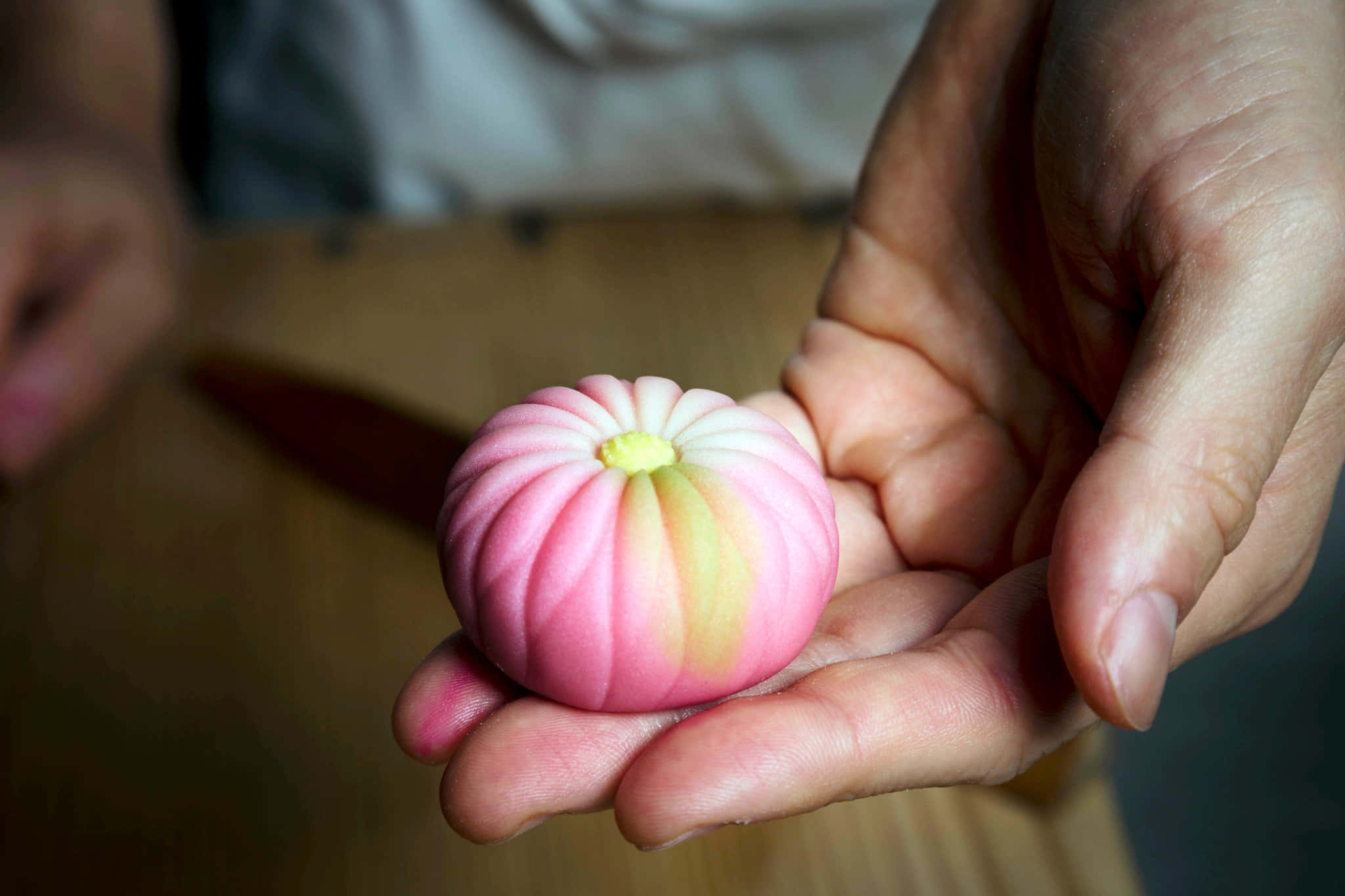 Japanese Sweets 桌布 壁紙 — 一隻手捧著精緻的粉黃色分層日式麻糬甜品，背景柔和。
