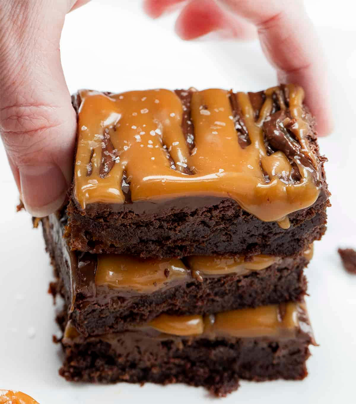 Caramel Brownie 桌布 壁紙 — 一隻手提起一疊濃郁的軟心朱古力布朗尼，層層夾著閃亮的焦糖醬和片狀海鹽。