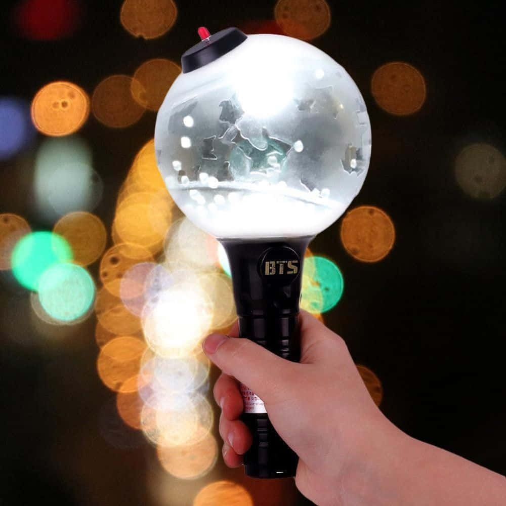 Bts Army Bomb 桌布 壁紙 — 一隻手握住一個發光的BTS應援棒，上面有星星鏤空圖案，背景是色彩繽紛的散景。