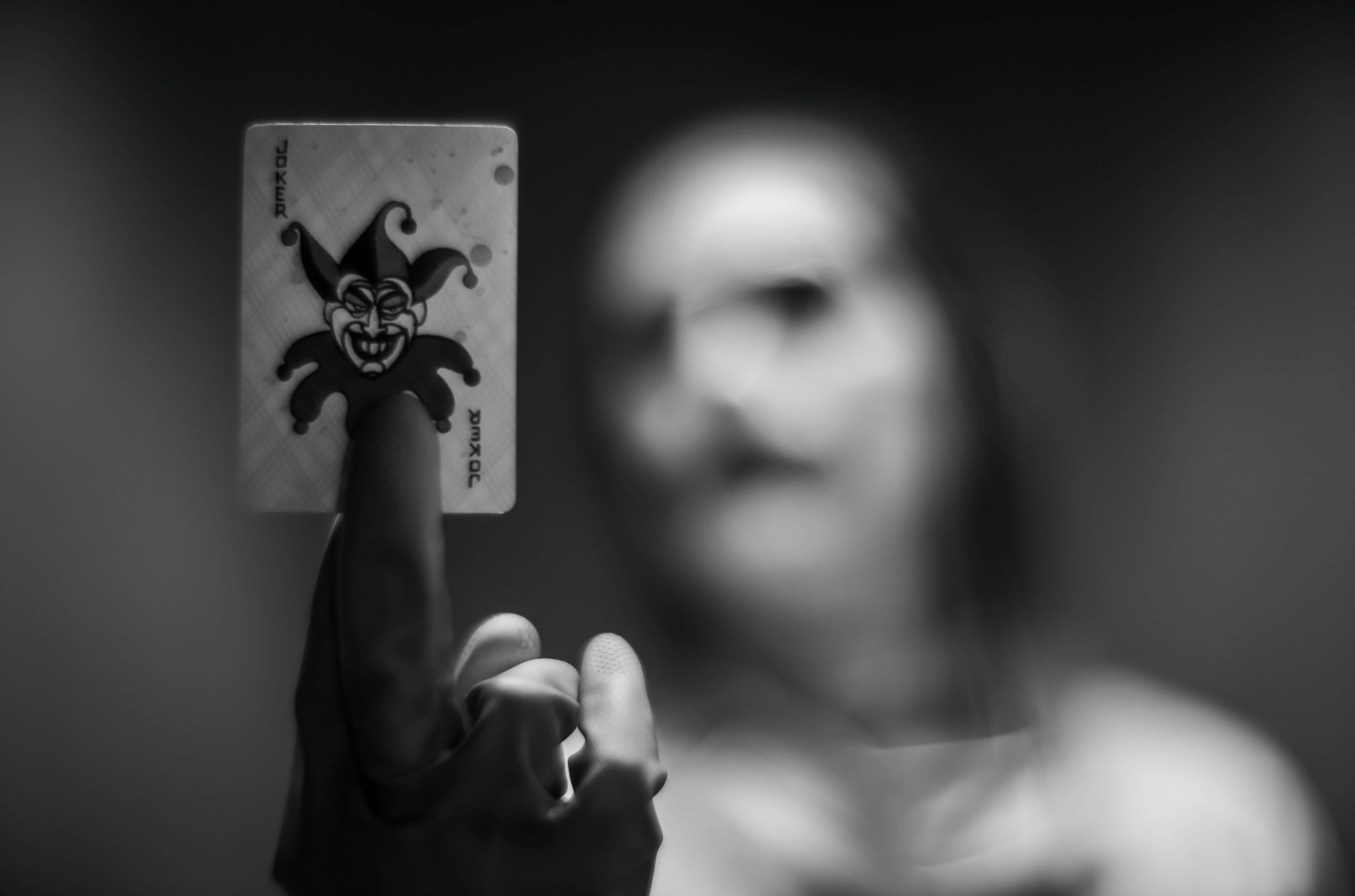 Joker Card 桌布 壁紙 — 一隻手清晰對焦地拿著一張小丑啤牌，而一個模糊的人影在背後以單色呈現。