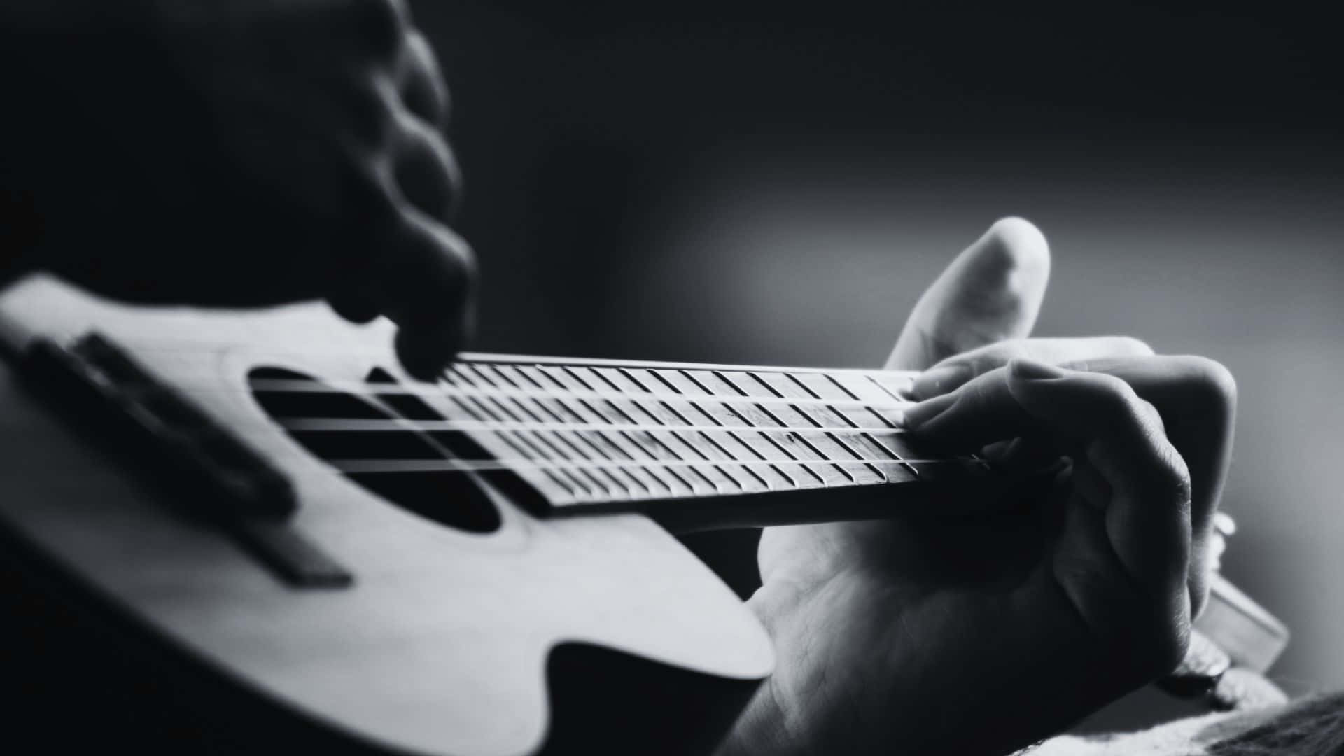 Black And White Guitar 桌布 壁紙 — 一隻手熟練地彈奏烏克麗麗的黑白特寫，手指按壓琴弦於琴格上。