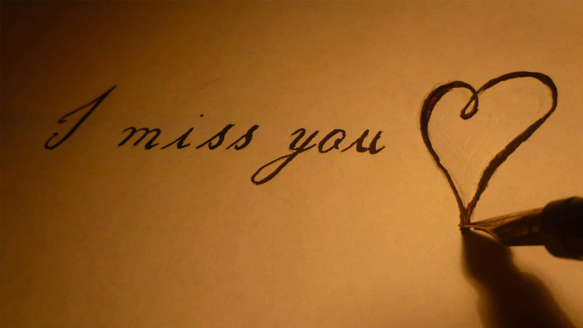 I Miss You 桌布 壁紙 — 一隻手用鋼筆在暖色調紙張上柔和燈光下，於心形旁邊寫上「I miss you」。