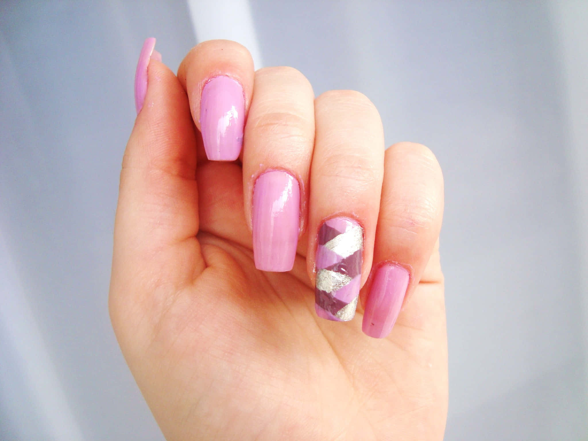 Pink Nails 桌布 壁紙 — 一隻手的特寫，帶有柔和的粉紅色指甲，其中一個帶有幾何紫色和銀色設計。