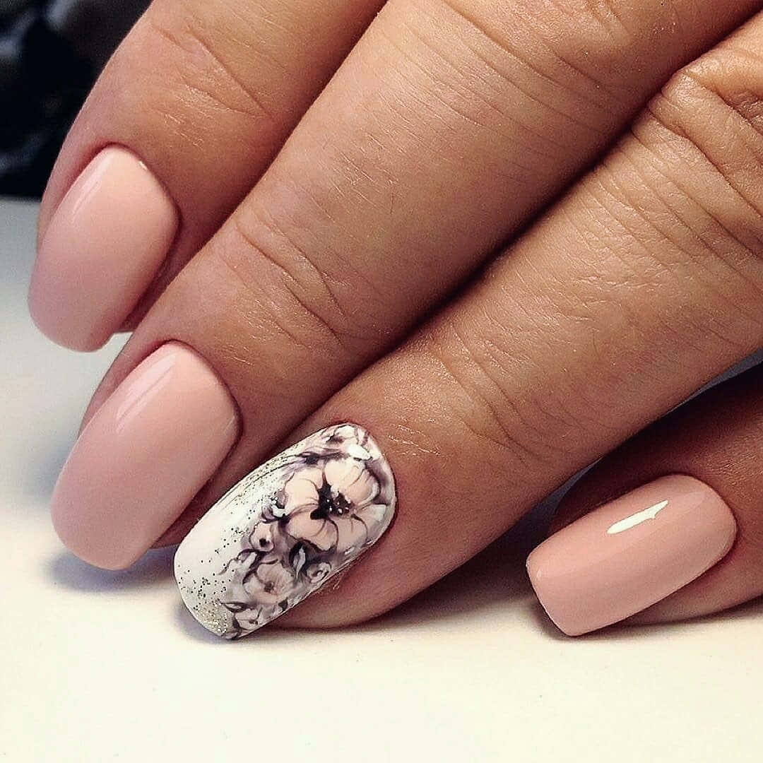 Spring Nails 桌布 壁紙 — 一隻手的特寫，帶有柔和粉紅色指甲，其中一隻重點指甲帶有精緻的黑白花卉設計和閃粉。