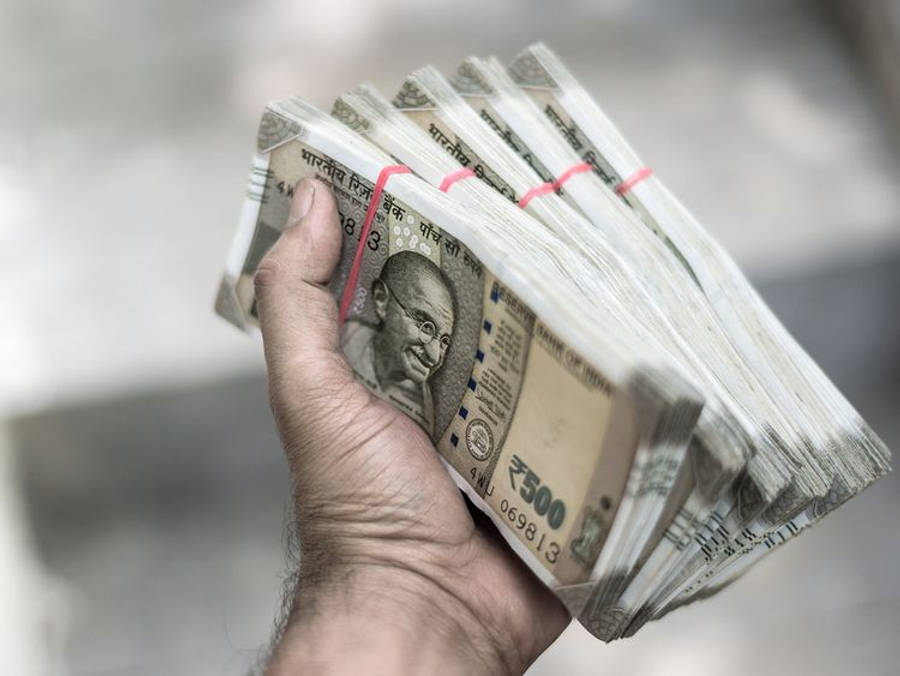 Indian 桌布 壁紙 — 一隻手緊緊抓住一疊厚厚的印度500盧比鈔票，用紅色帶子捆綁，背景是模糊的城市景觀。
