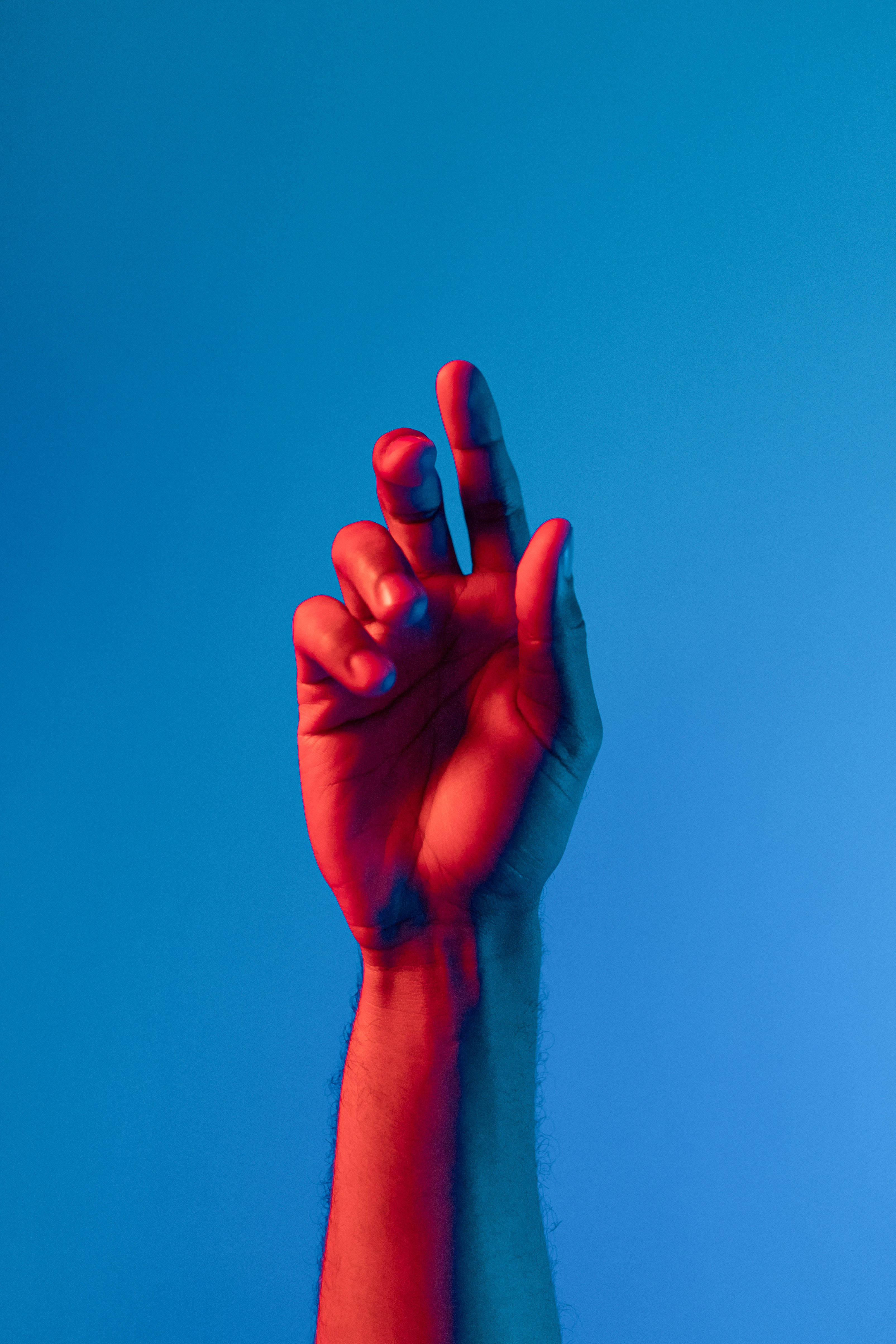 hands up 桌布 壁紙 — 一隻手舉起在純藍色背景前，沐浴在戲劇性的紅色和藍色燈光中。