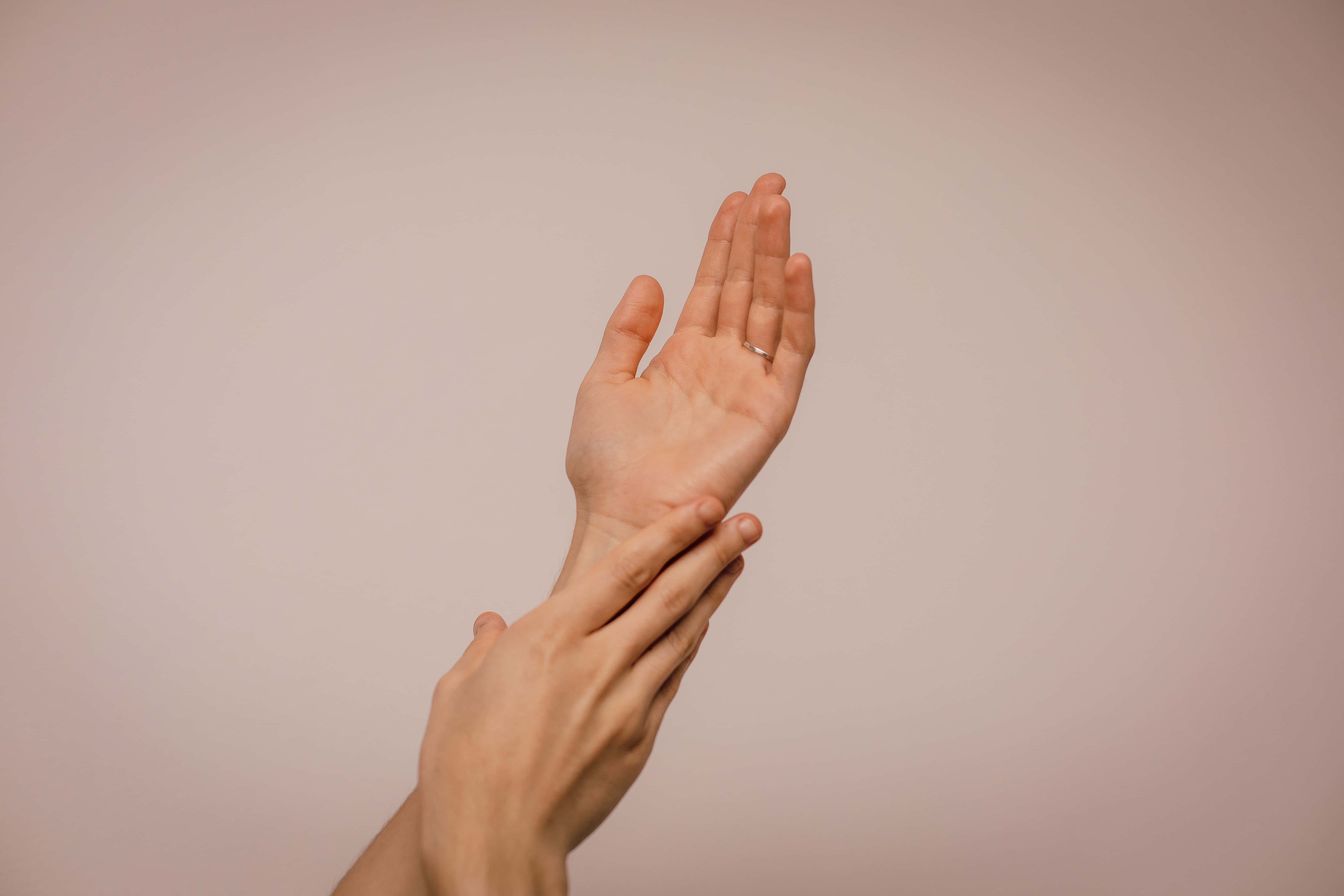 hands 桌布 壁紙 — 一隻手輕柔按摩另一隻手的手腕的特寫，背景為柔和粉紅色。