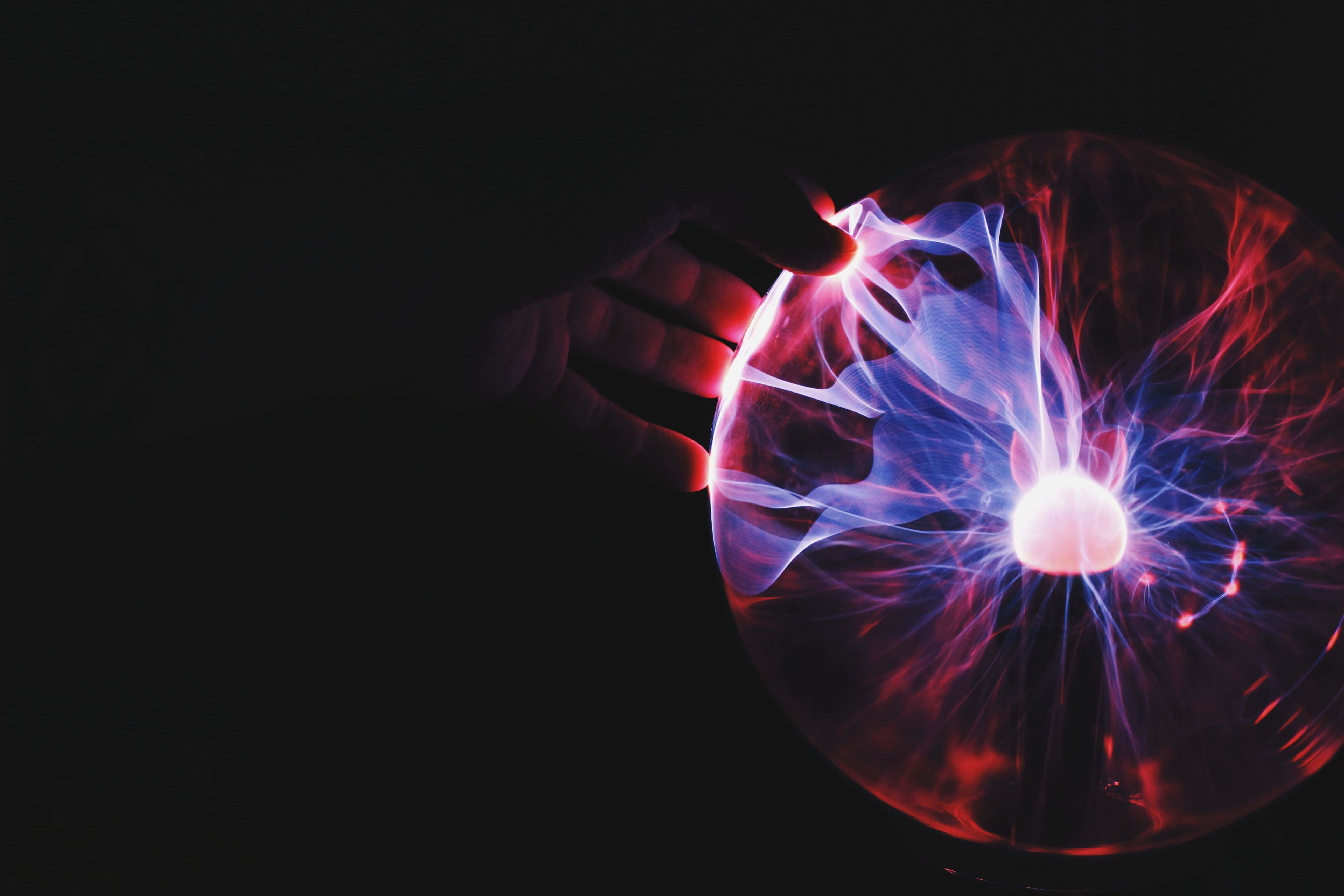 Plasma 桌布 壁紙 — 一隻手輕輕觸摸一個發光的等離子球體，在黑色背景下發出鮮豔的紅色和藍色電絲。