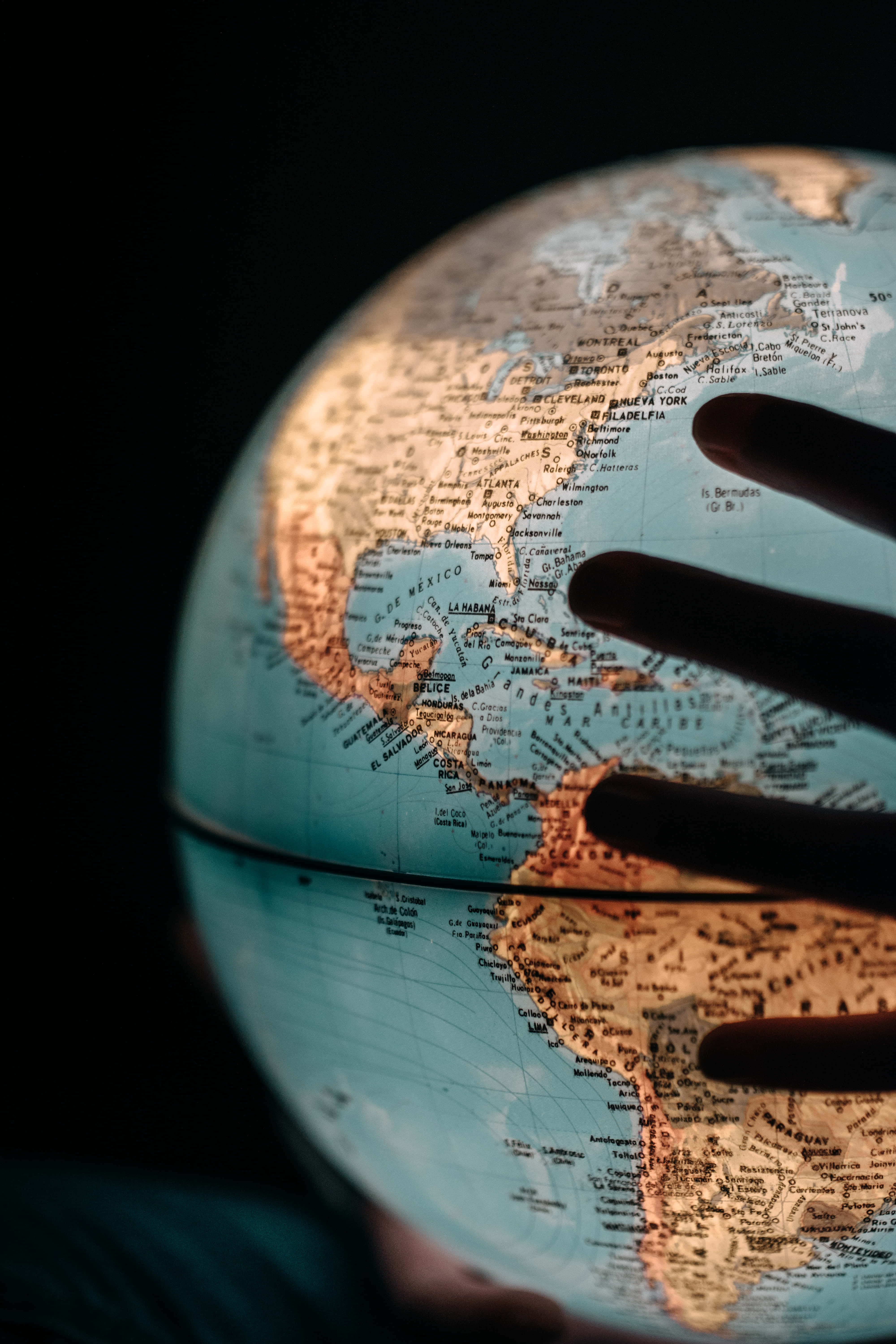World 桌布 壁紙 — 一隻手輕輕觸碰一個在黑暗背景下、溫暖環境光中突出北美洲的地球儀。