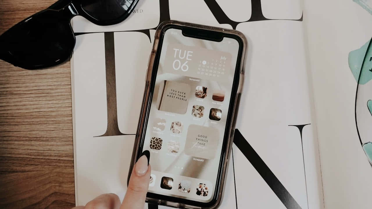 iPhone風格壁紙 桌布 壁紙 — 一隻手輕點一部智能手機，屏幕上顯示一個簡約風格的牆紙，包含日曆和應用程式圖標，手機放在木桌上的一本雜誌上。