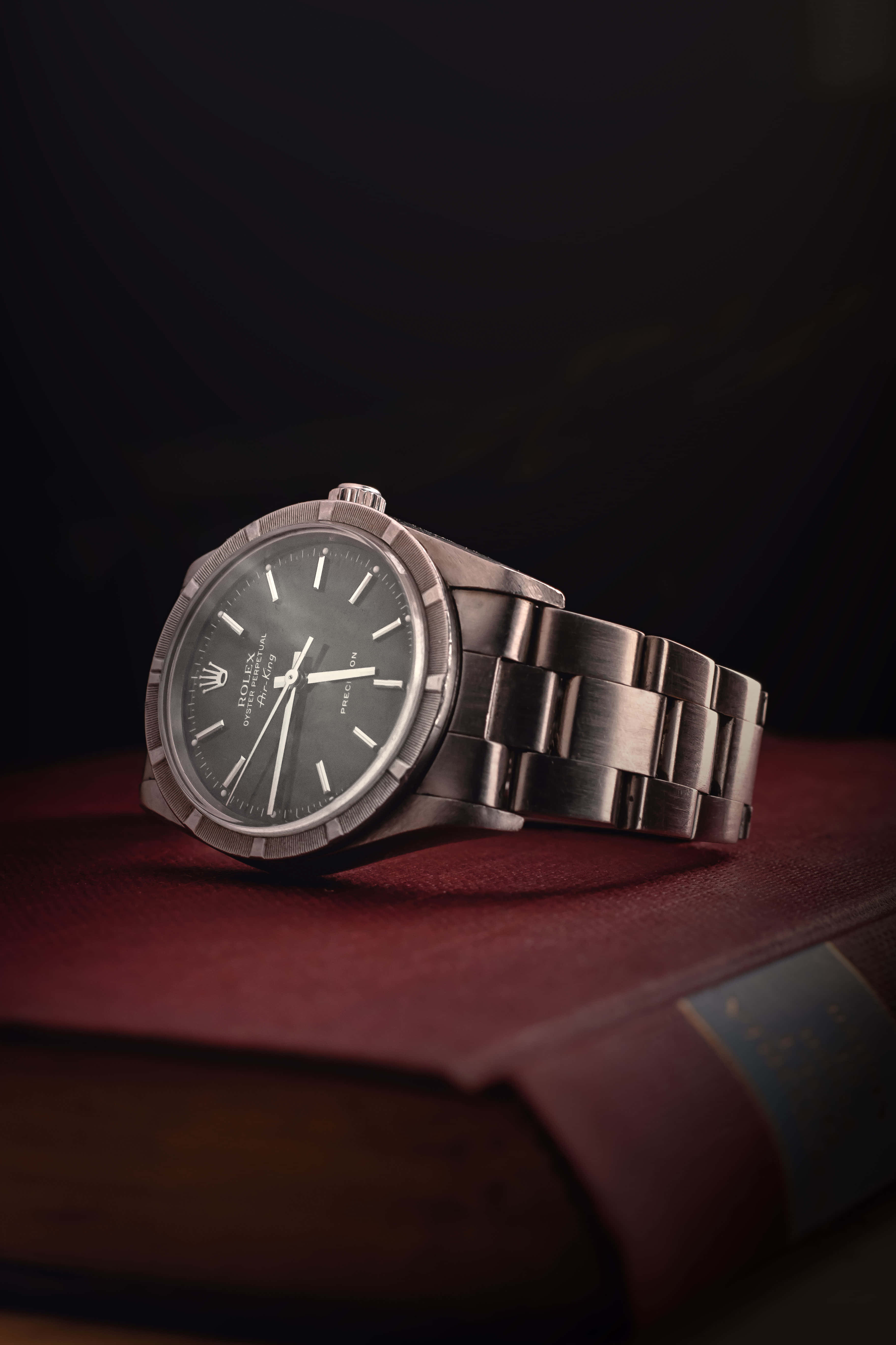 Rolex 桌布 壁紙 — 一隻時尚的銀色勞力士手錶優雅地放在深色背景上一本豐富的勃艮第皮革裝訂書上。
