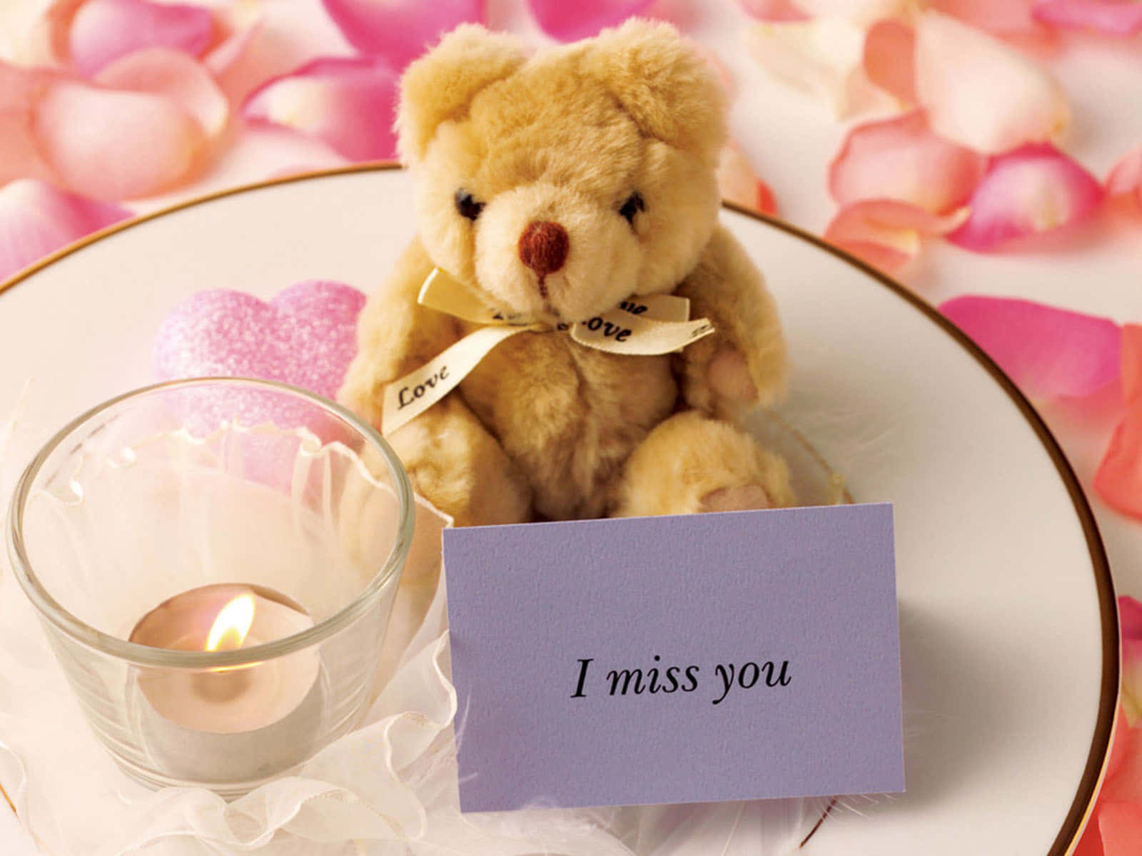 I Miss You 桌布 壁紙 — 一隻柔軟的泰迪熊繫著愛情絲帶，坐在一支點燃的蠟燭和一張寫著「我想你」的便條旁邊，放在一個被粉紅玫瑰花瓣包圍的碟子上。
