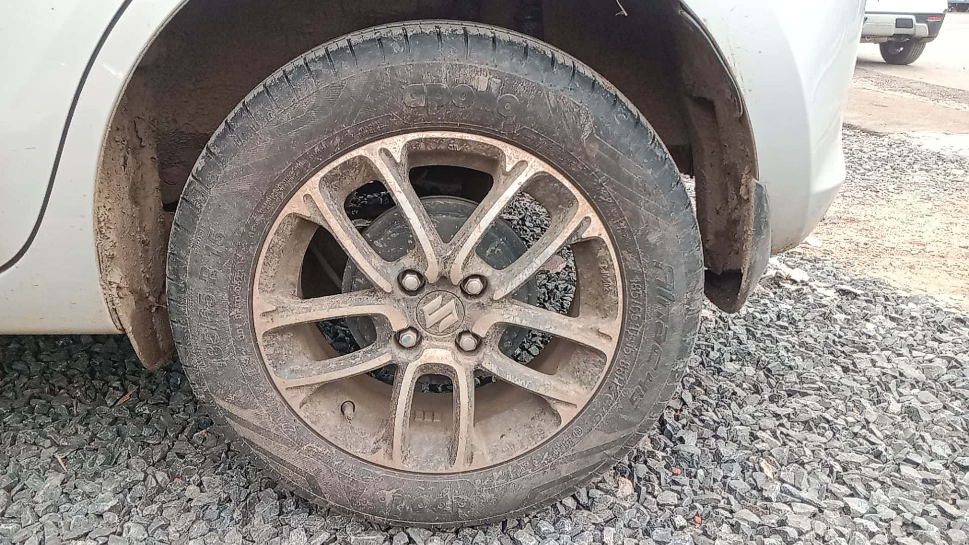一隻沾滿塵土的車胎 壁紙 — 泥濘汽車輪胎在礫石上的特寫，可見輪胎花紋及合金輪圈細節。