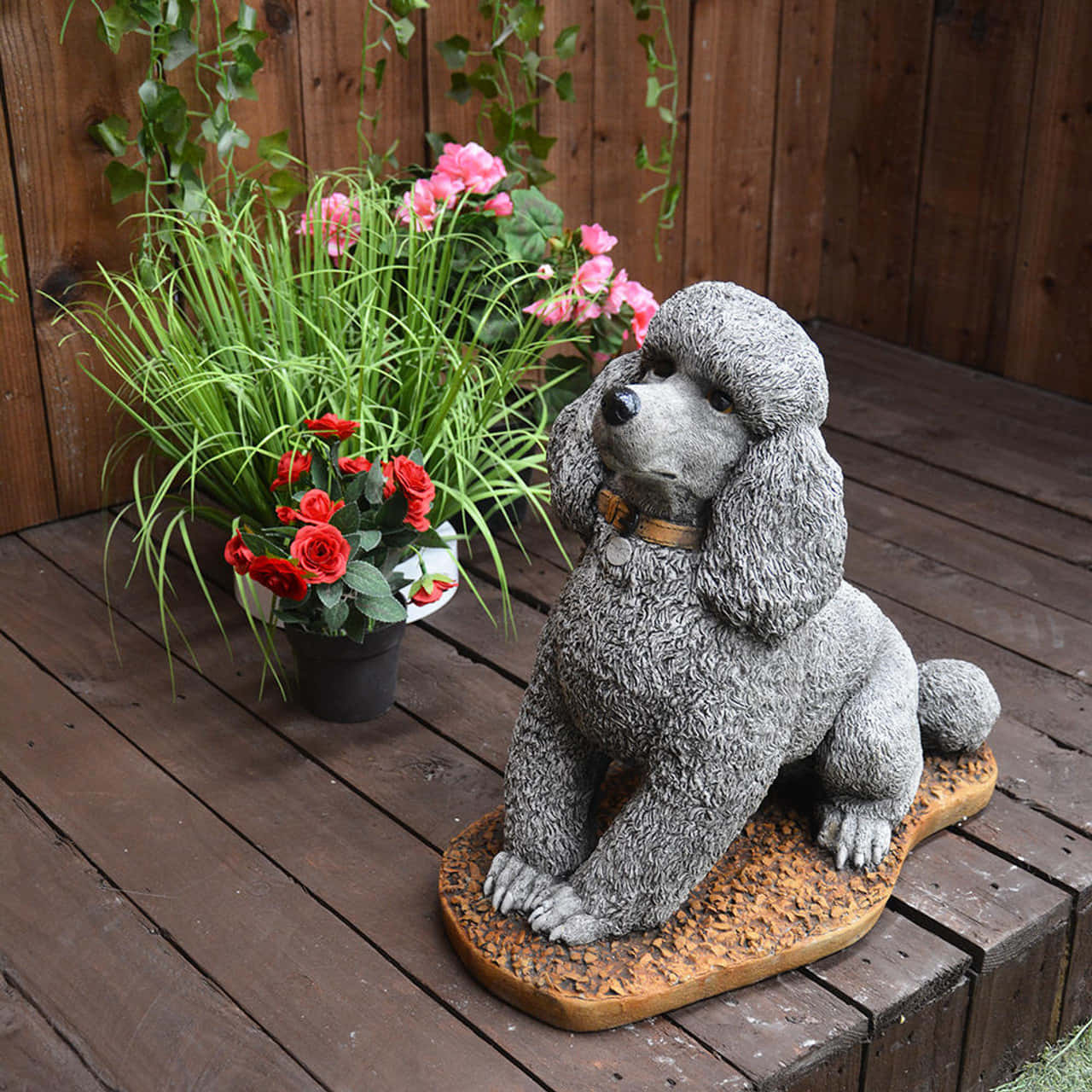 Poodle 桌布 壁紙 — 一隻灰色石獅子狗雕像靜靜地坐在木甲板上，旁邊是盆栽紅玫瑰和綠色植物。