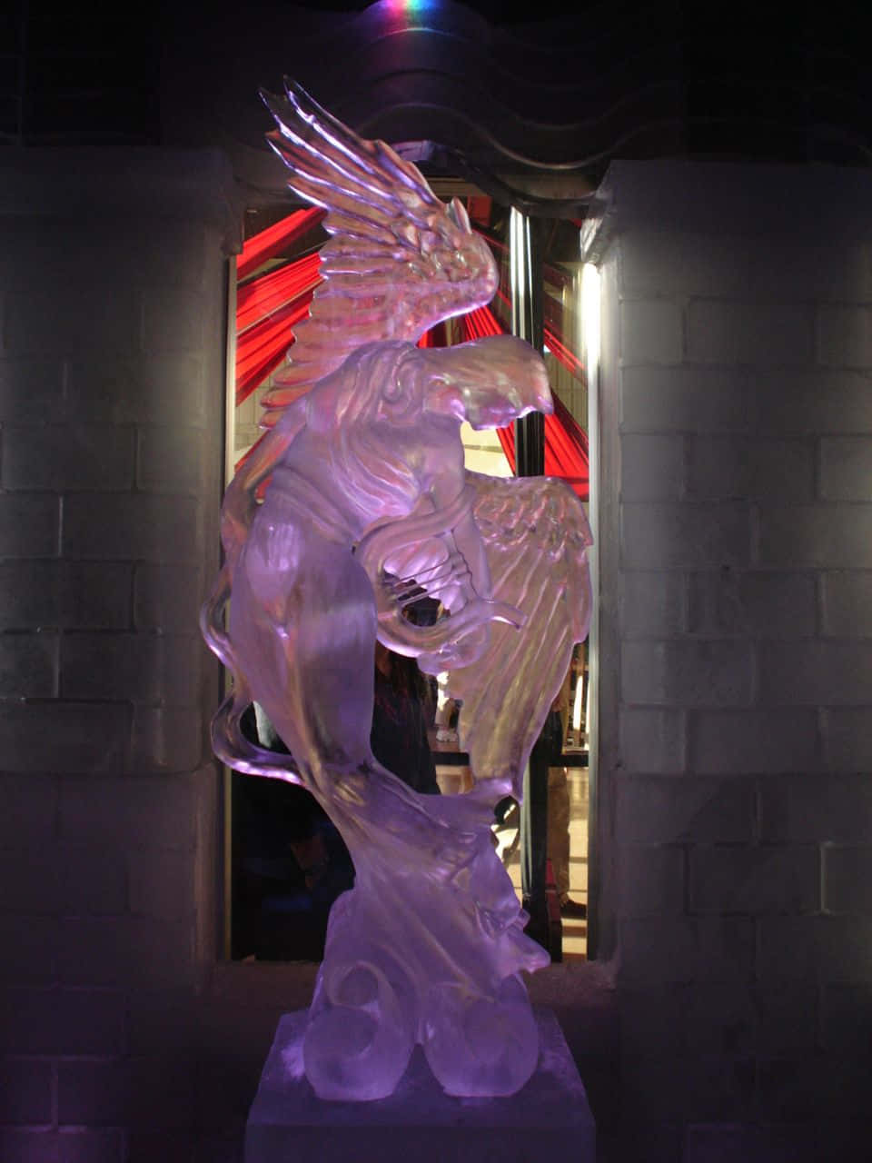 Ice Sculpture 桌布 壁紙 — 一隻發光紫色冰雕的有翼獅鷲矗立在黑暗的石拱門中，背後有紅色窗簾。