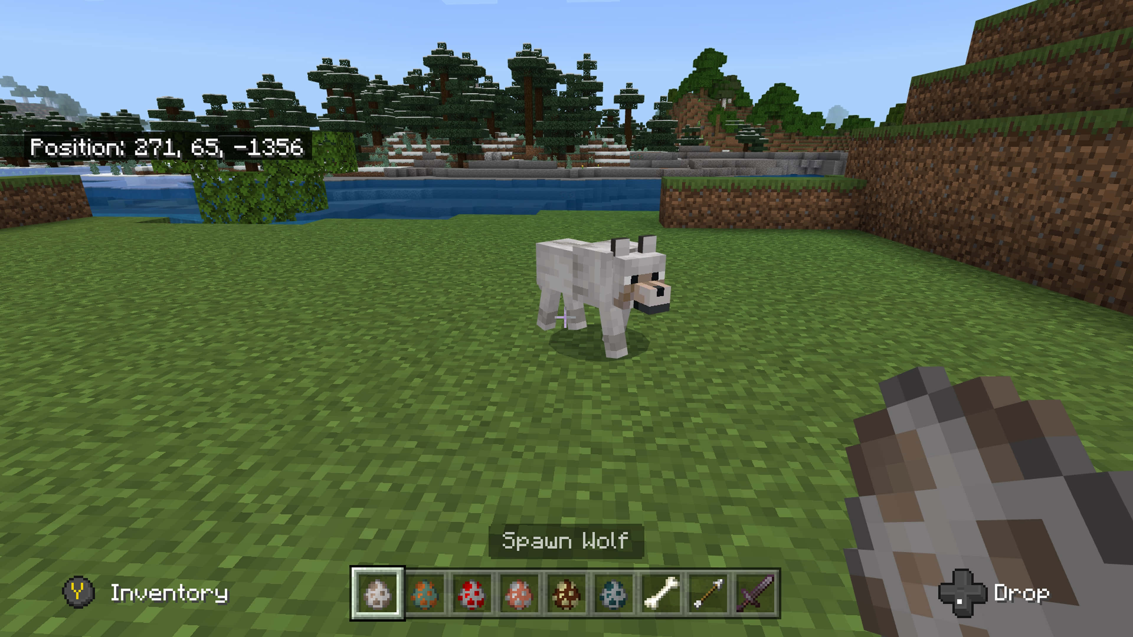 Minecraft Wolf 桌布 壁紙 — 一隻白狼喺一個有樹木同山丘嘅方塊Minecraft世界入面，企喺水邊嘅草地上，天空晴朗。