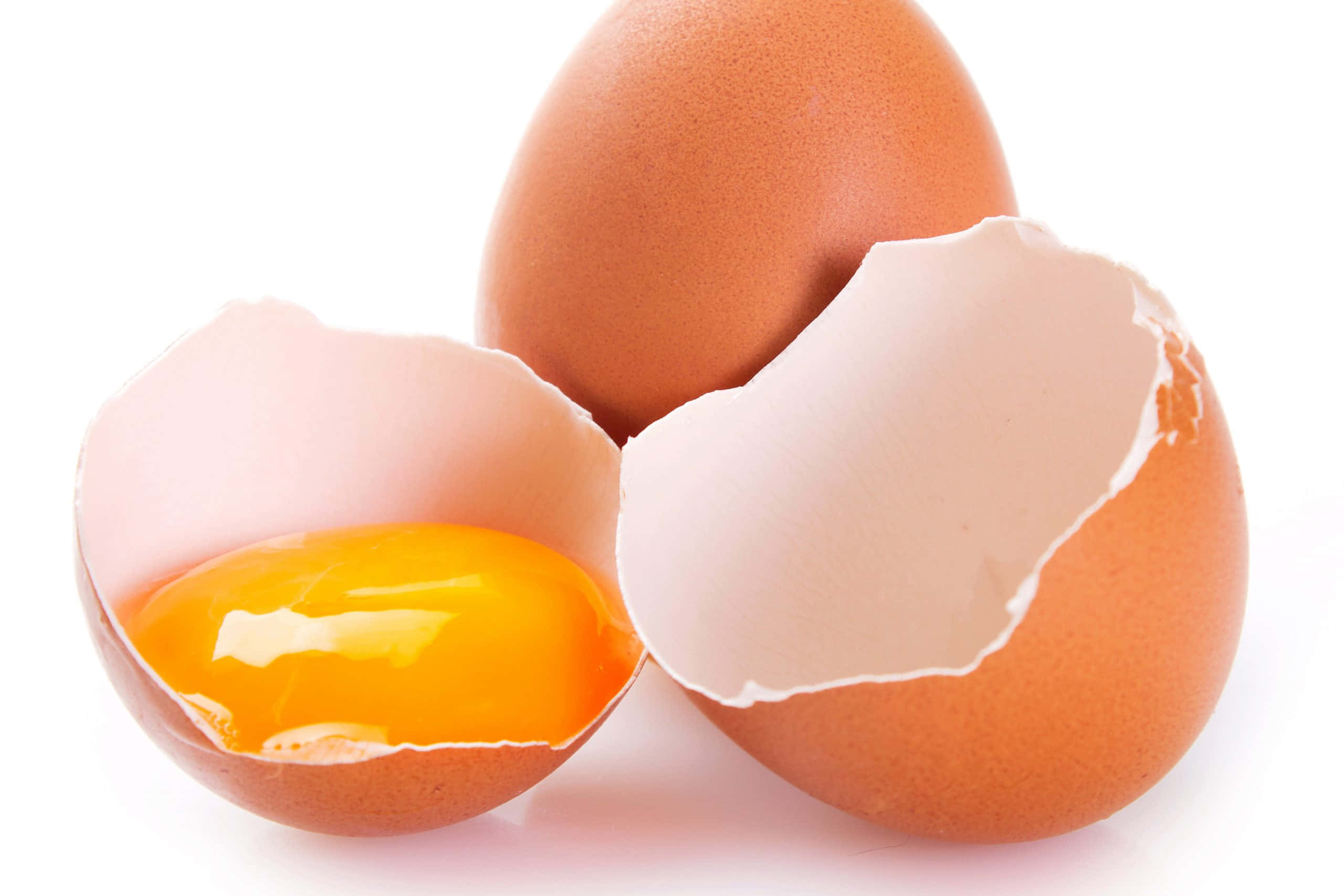 Eggshell 桌布 壁紙 — 一隻破裂的棕色雞蛋在純白背景上露出鮮黃色的蛋黃，旁邊還有另一顆完整的雞蛋。
