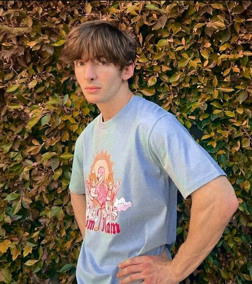 年輕男子身穿藍色T恤站在綠色籬笆旁