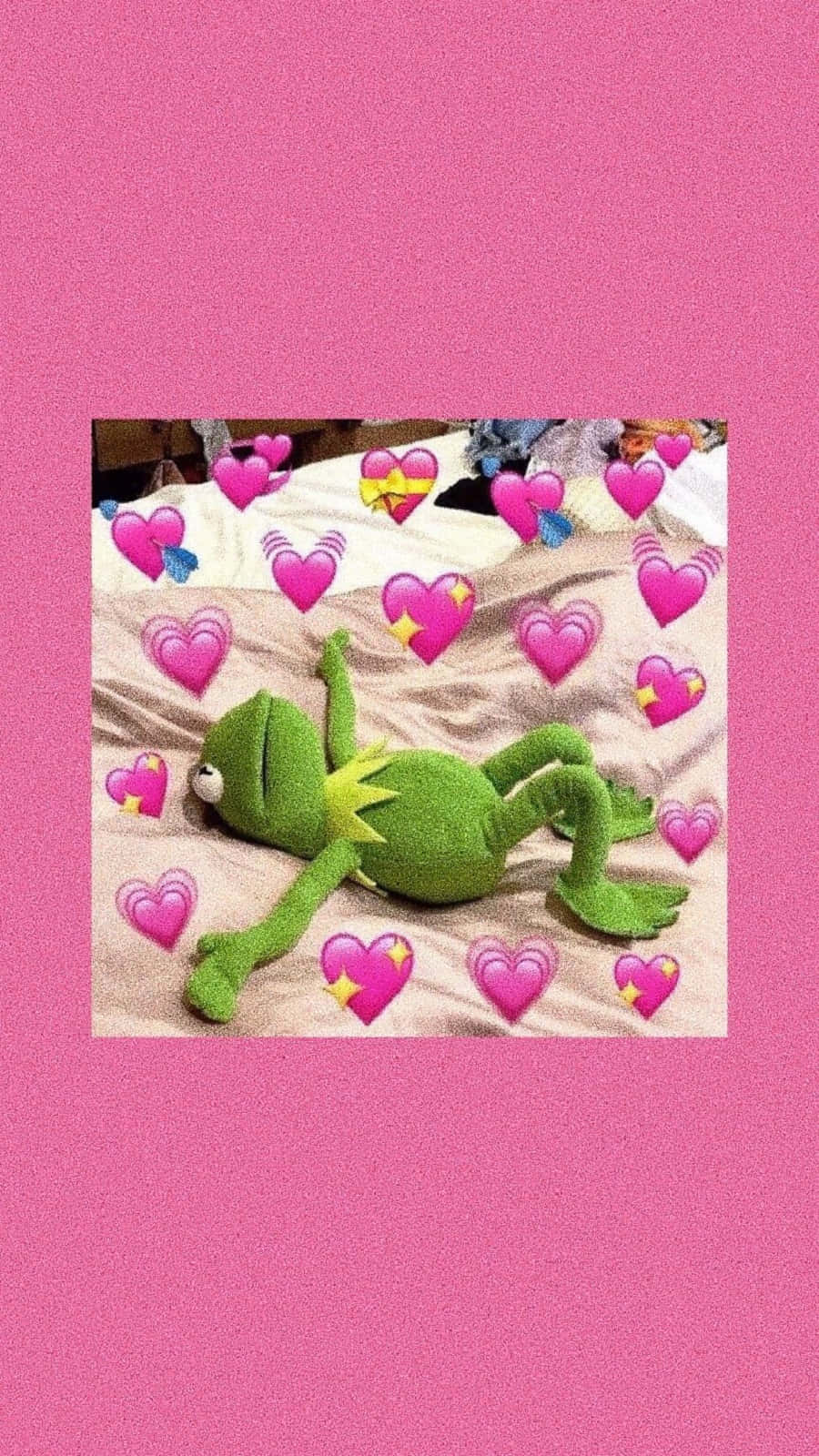 Cute Frog 桌布 壁紙 — 一隻綠色Kermit the Frog毛公仔放鬆地躺在床上，周圍漂浮著粉紅色心形表情符號，背景為純粉紅色。