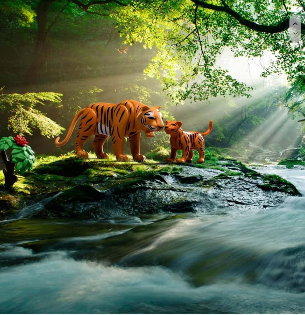 3d Animal 桌布 壁紙 — 一隻老虎媽媽和她的幼崽站在長滿苔蘚的石頭上，旁邊是一條湍急的小溪，陽光穿透樹冠灑落在森林中。