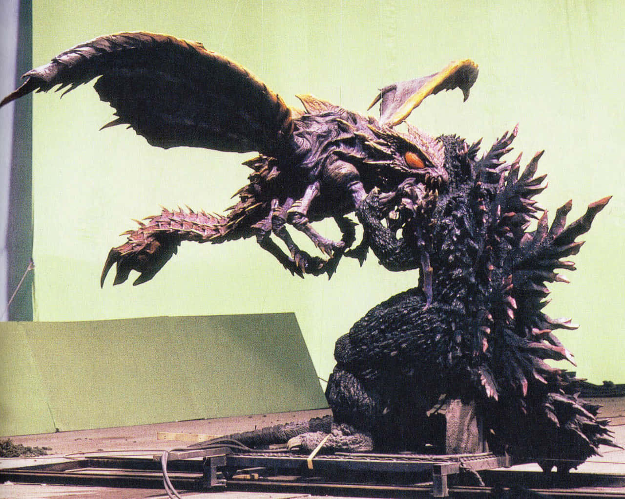 Godzilla Vs Megaguirus 桌布 壁紙 — 一隻背脊有刺、有翼嘅哥斯拉式怪獸喺綠幕場景攻擊一隻較細嘅龍形怪獸。
