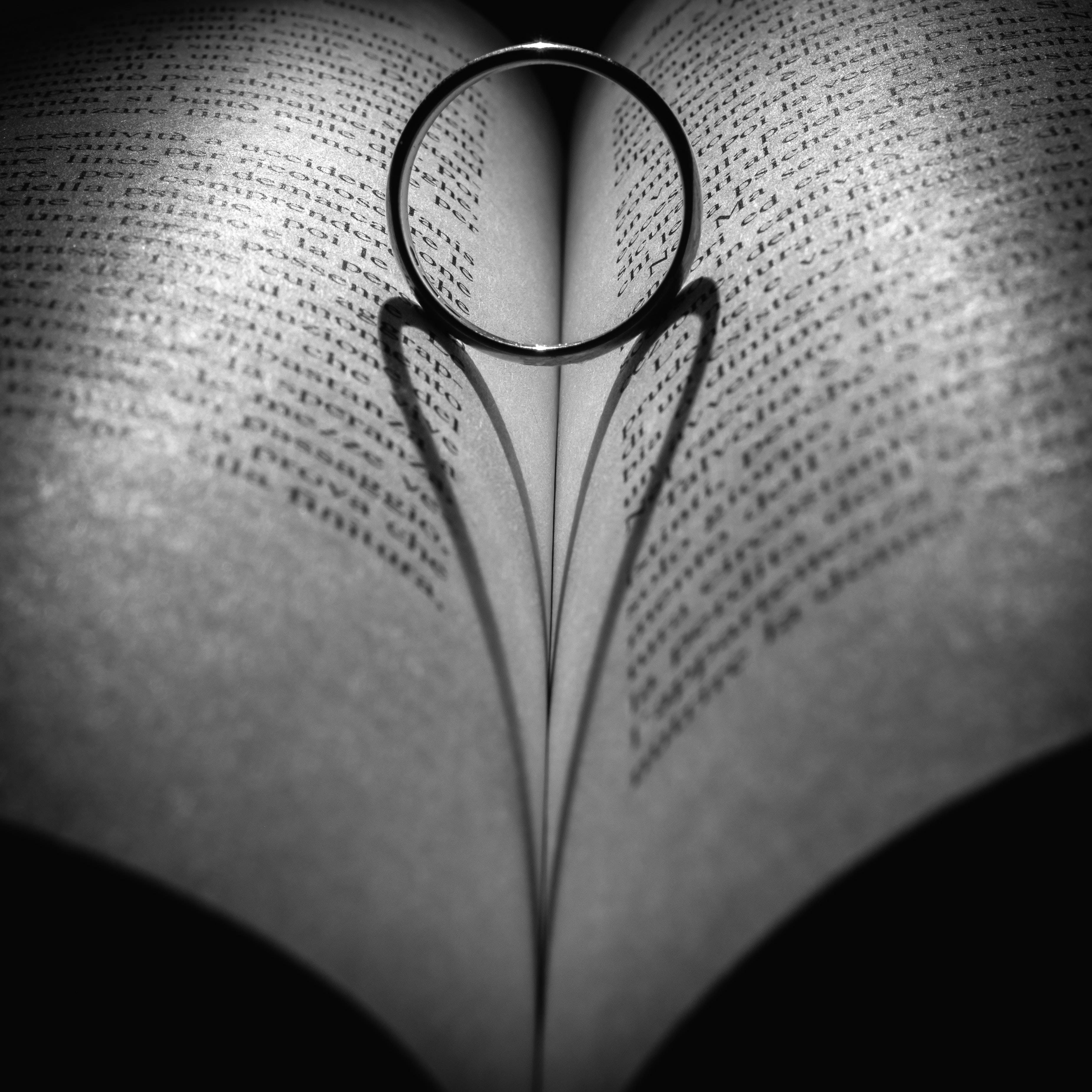 Love Black And White 桌布 壁紙 — 一隻銀戒指放在一本打開的心形書本上，書頁帶有陰影，單色調。