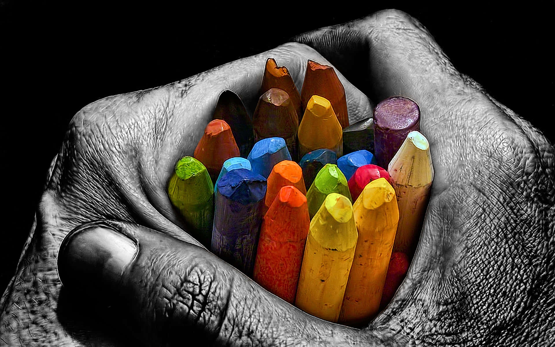 crayon 桌布 壁紙 — 一隻飽經風霜的手捧著色彩繽紛的粉筆，襯托在純黑背景上。