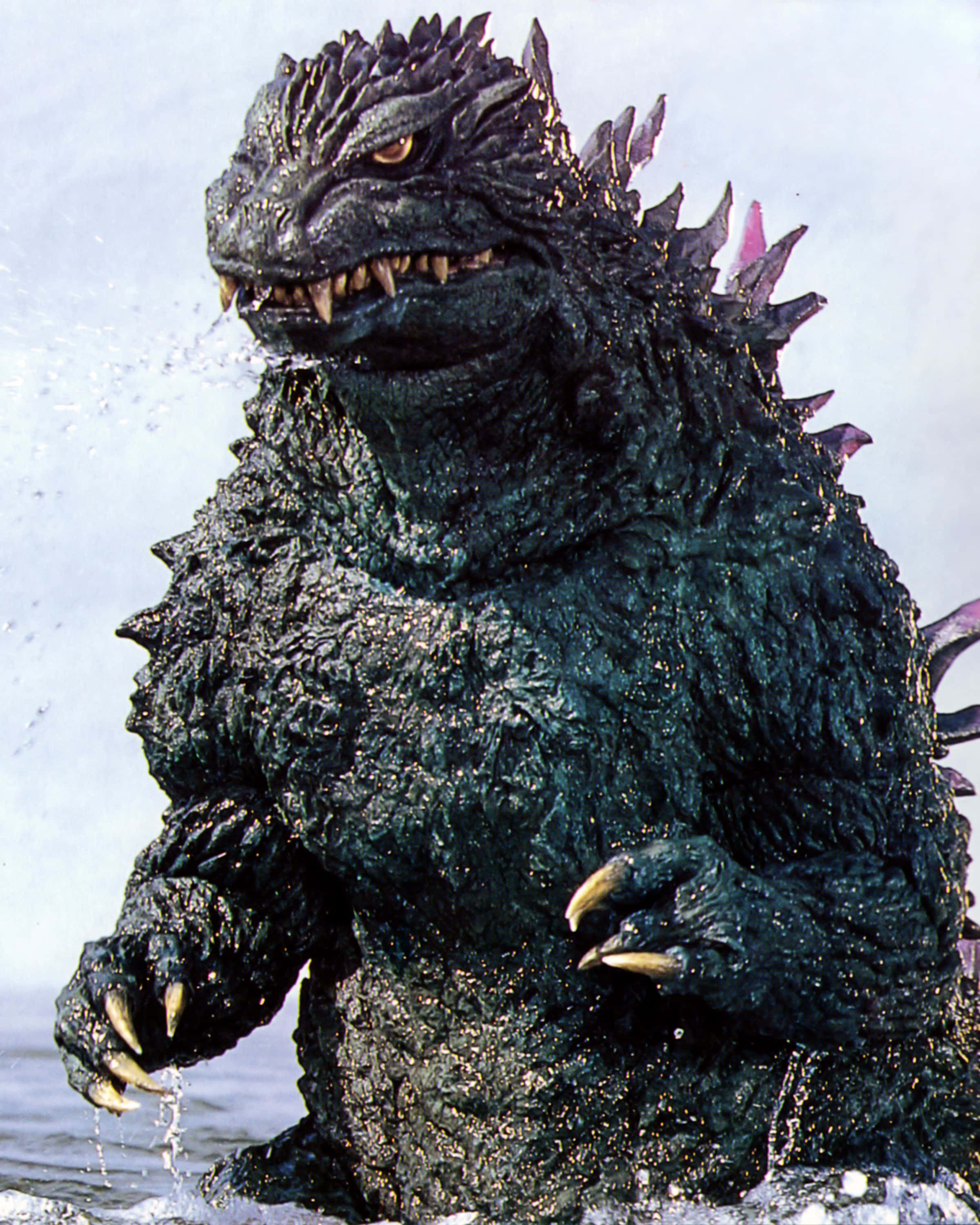 Godzilla 2000 桌布 壁紙 — 一隻高聳的哥斯拉從洶湧的海水中出現，帶有尖刺的背鰭和發光的眼睛。