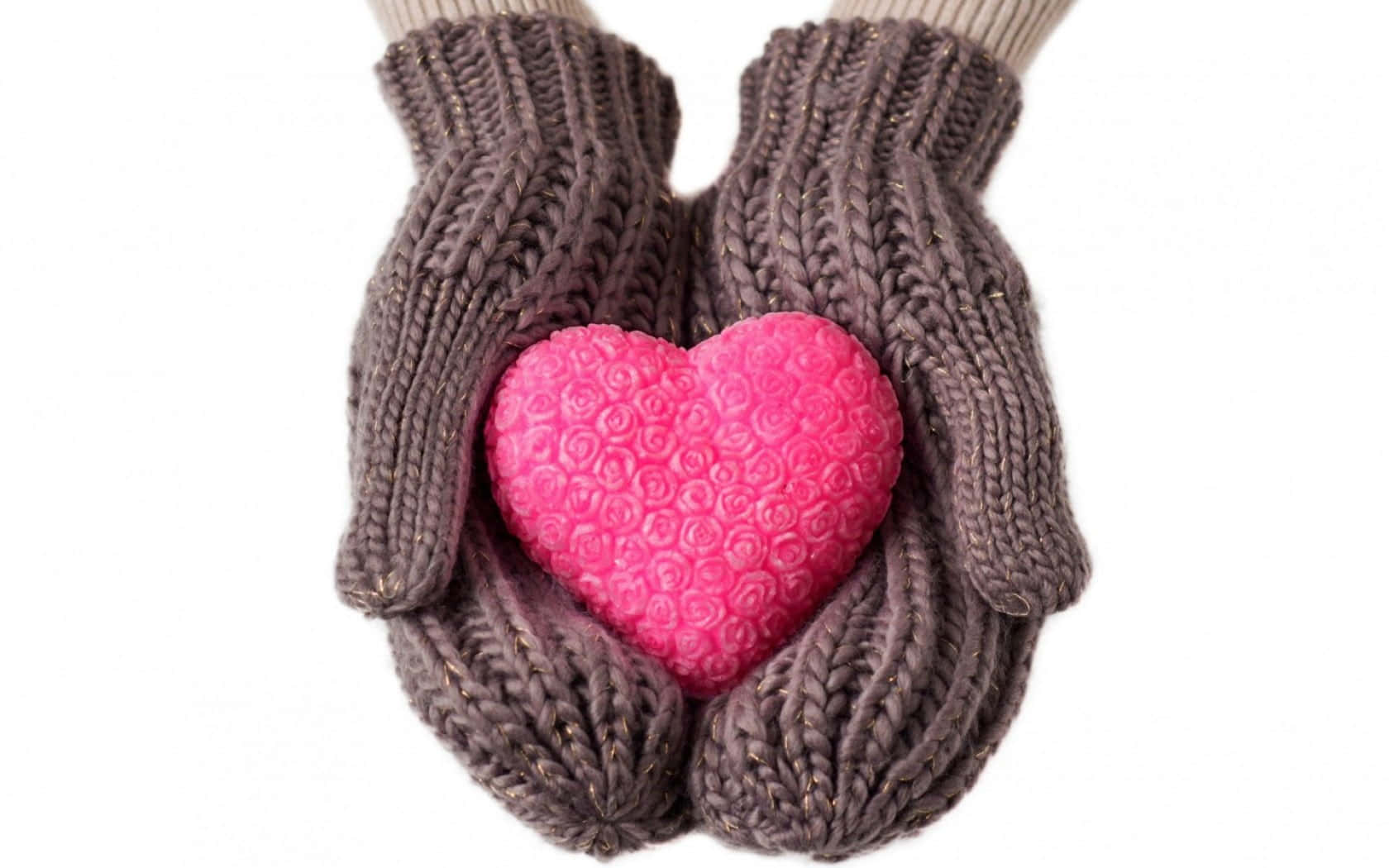 Mittens 桌布 壁紙 — 一雙手戴著舒適的棕色針織手套，輕輕捧著一個有紋理的亮粉紅色心形物體，背景是潔淨的白色。