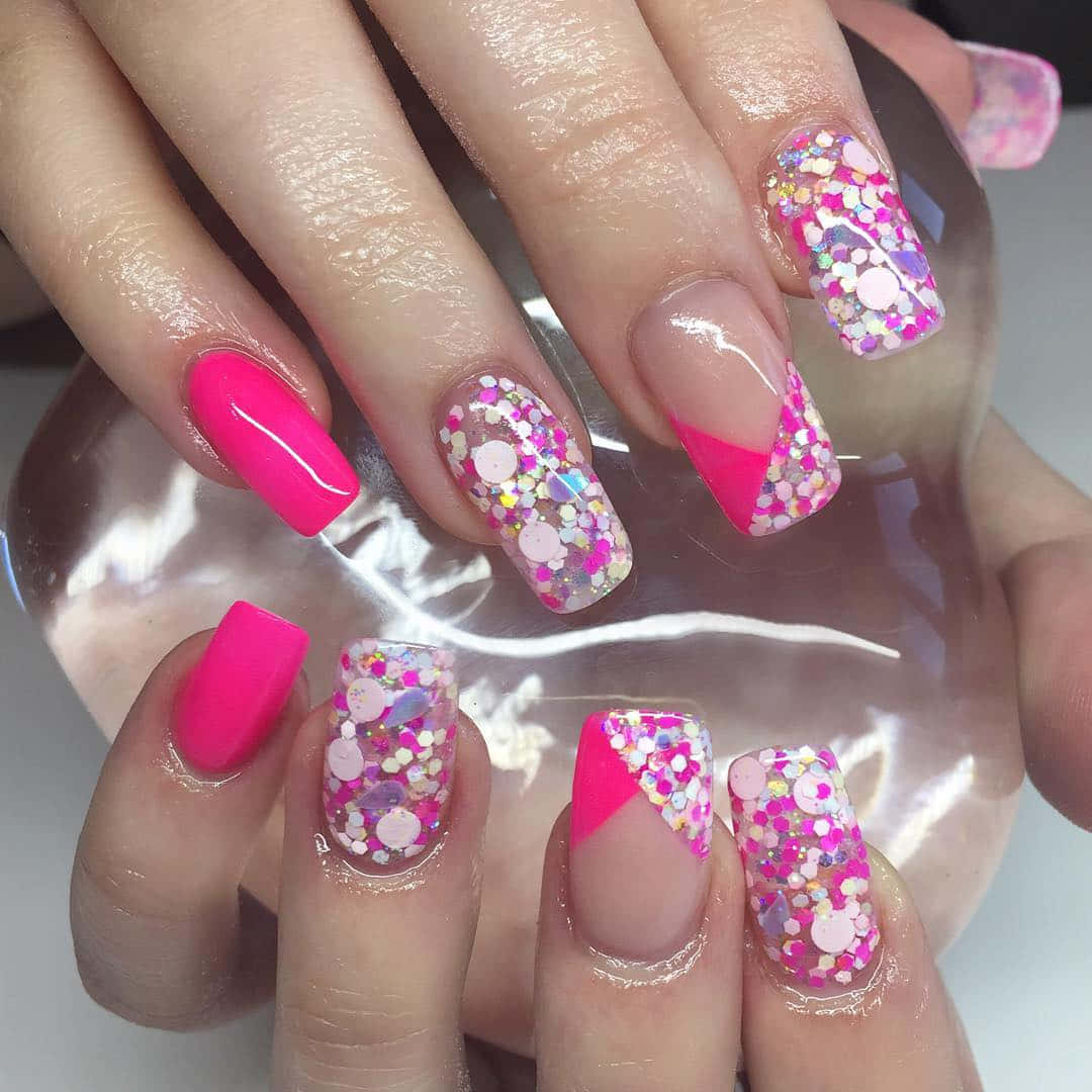Pink Nail Art 桌布 壁紙 — 一雙手的特寫，帶有充滿活力的粉紅色指甲，飾有彩色閃粉和幾何圖案。