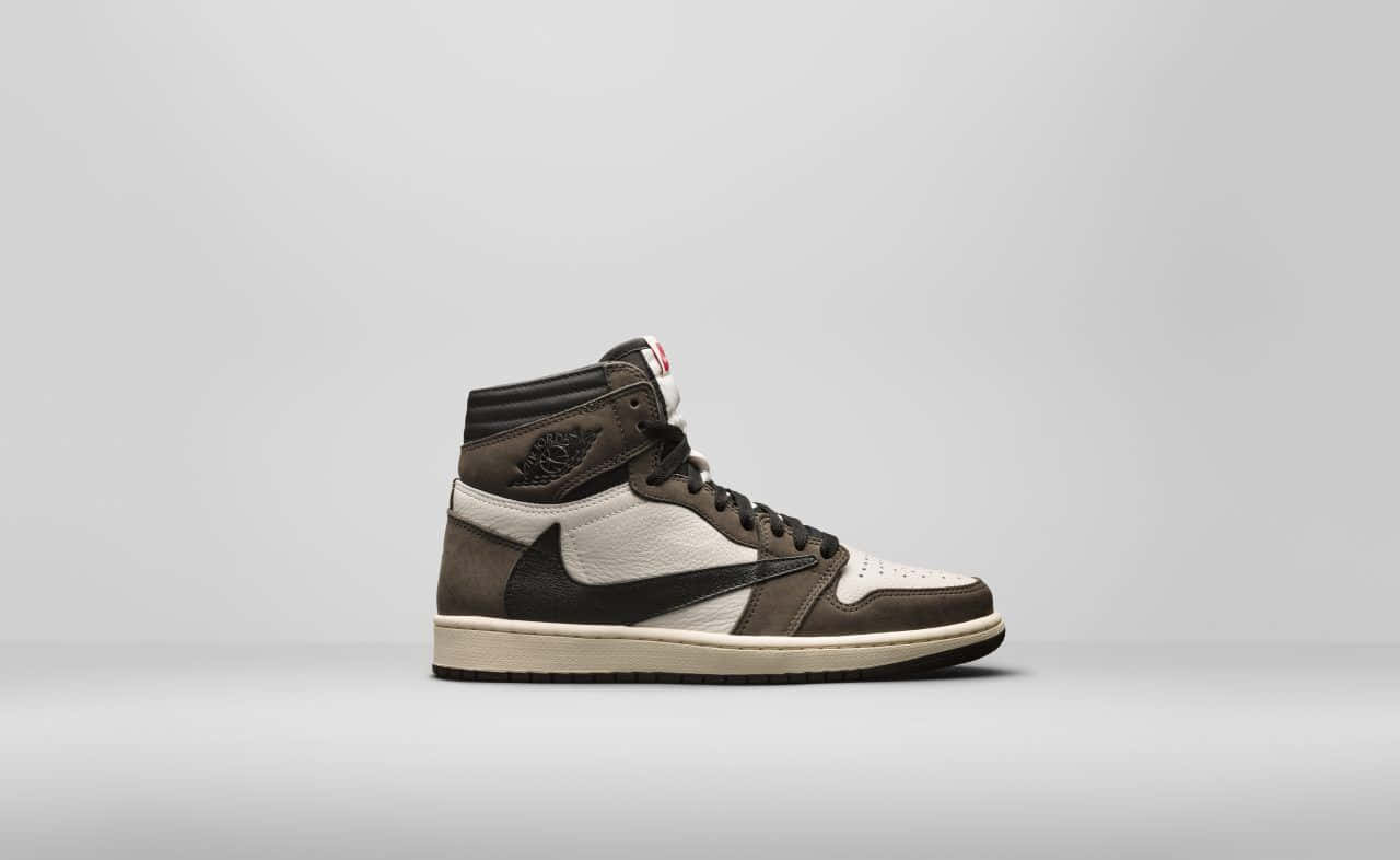 Travis Scott Jordan 1 桌布 壁紙 — 一雙時尚的棕白色高筒運動鞋獨自站在極簡灰色工作室背景前。