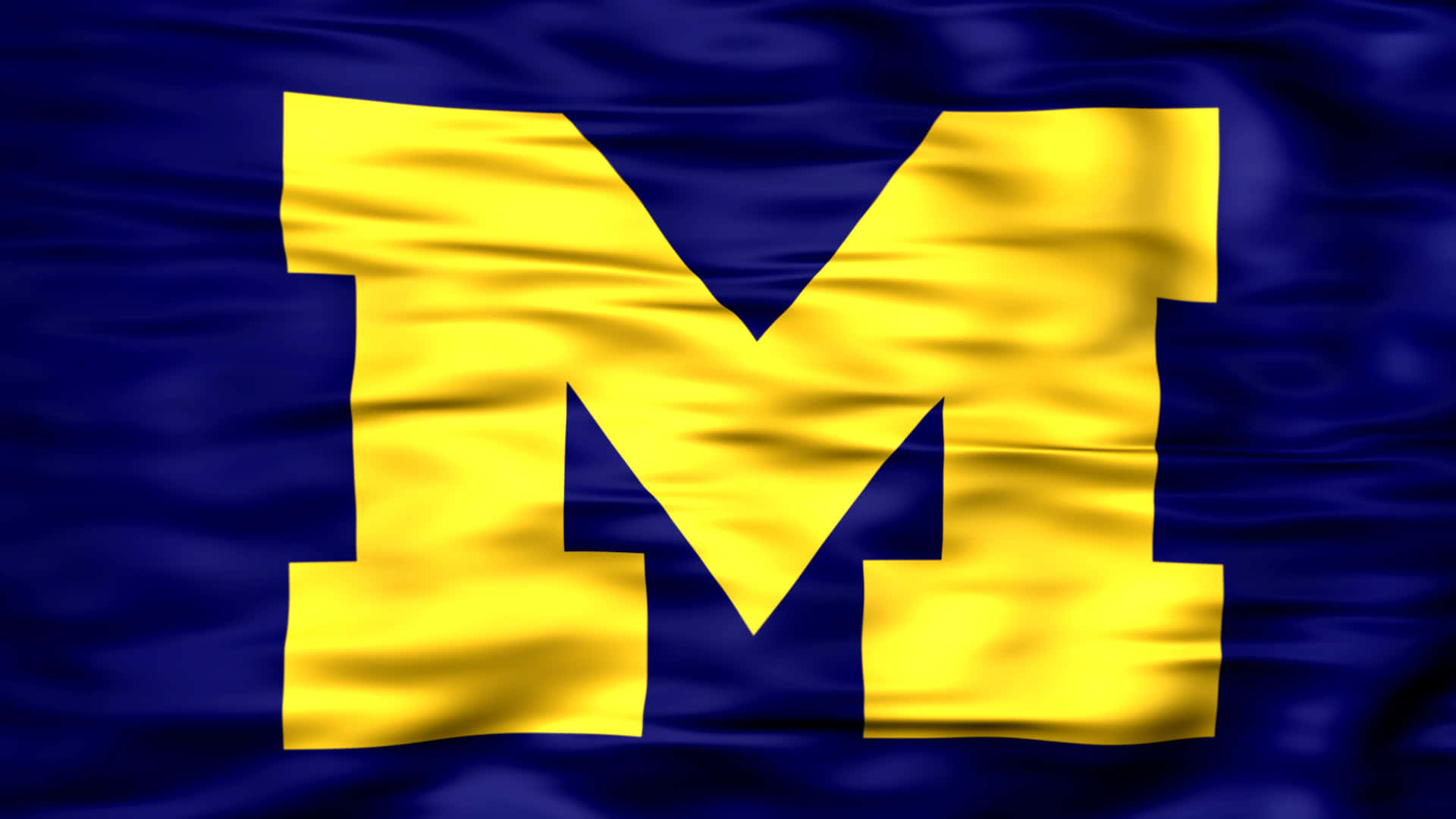 「Go Blue！」 壁紙 — 一面充滿活力的藍色旗幟，上面有一個大膽的黃色塊狀 M，在風中動態飄揚。